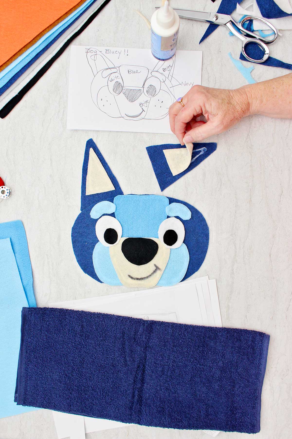 Colando à mão a parte branca interna da orelha para a fantasia do Bluey com outras peças de fantasia ao redor.