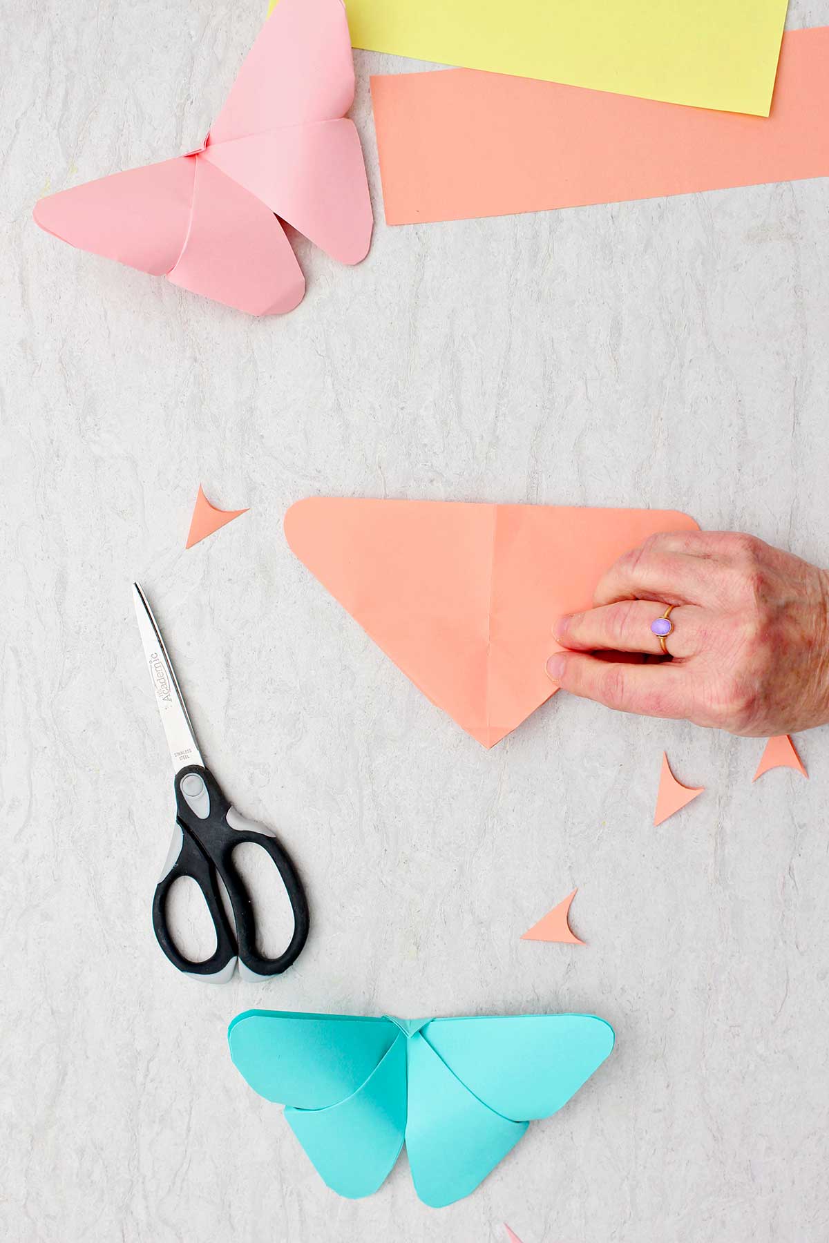 Uma pessoa dobrando uma folha de papel laranja na forma de um triângulo com o ponto superior voltado para baixo.