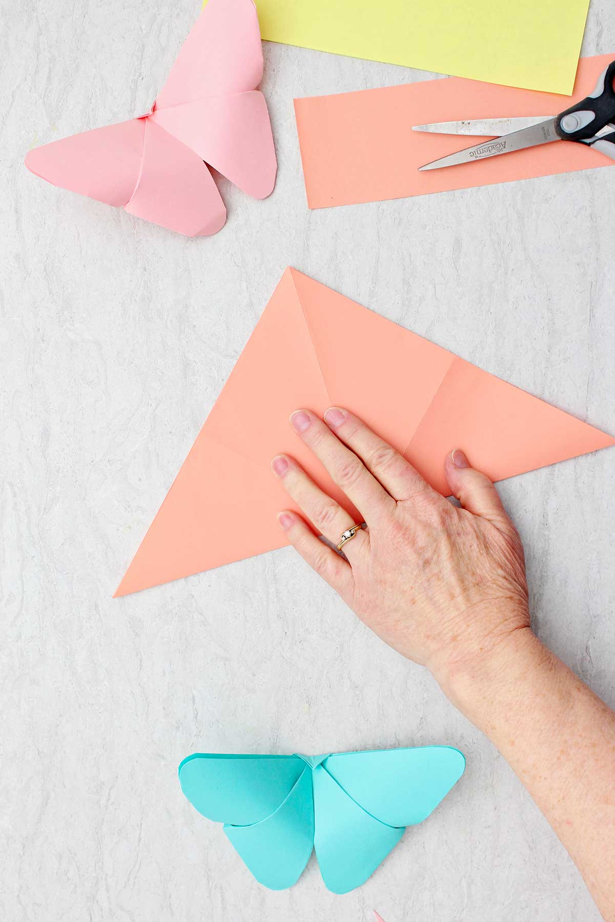 Uma pessoa dobrando uma folha de papel laranja na forma de um triângulo.