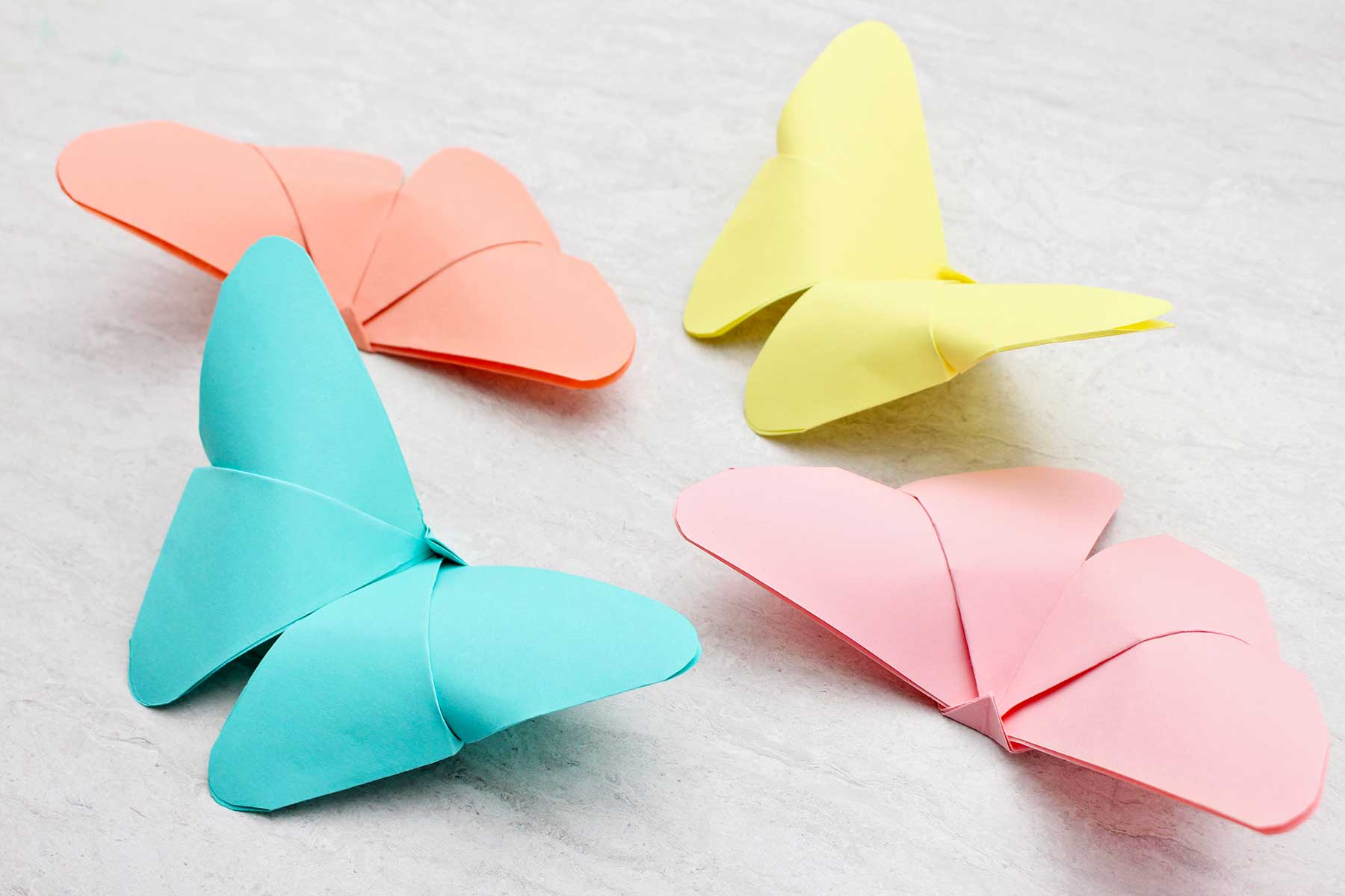 Quatro borboletas de origami em tons pastéis de azul, amarelo, laranja e rosa.