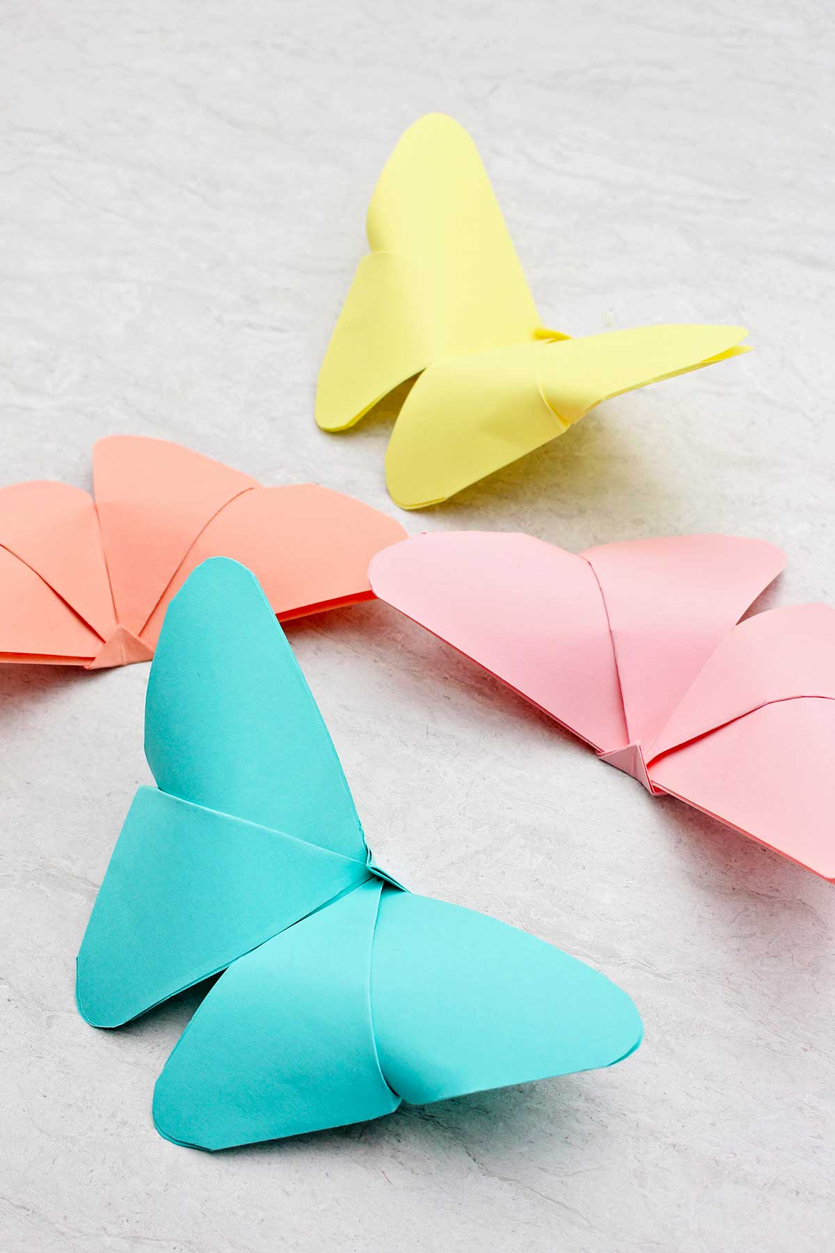 Quatro borboletas de origami em tons pastéis de azul, amarelo, laranja e rosa.
