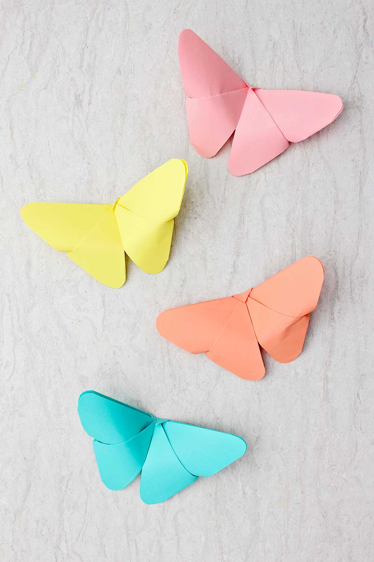 Quatro borboletas de origami em tons pastéis de azul, amarelo, laranja e rosa.
