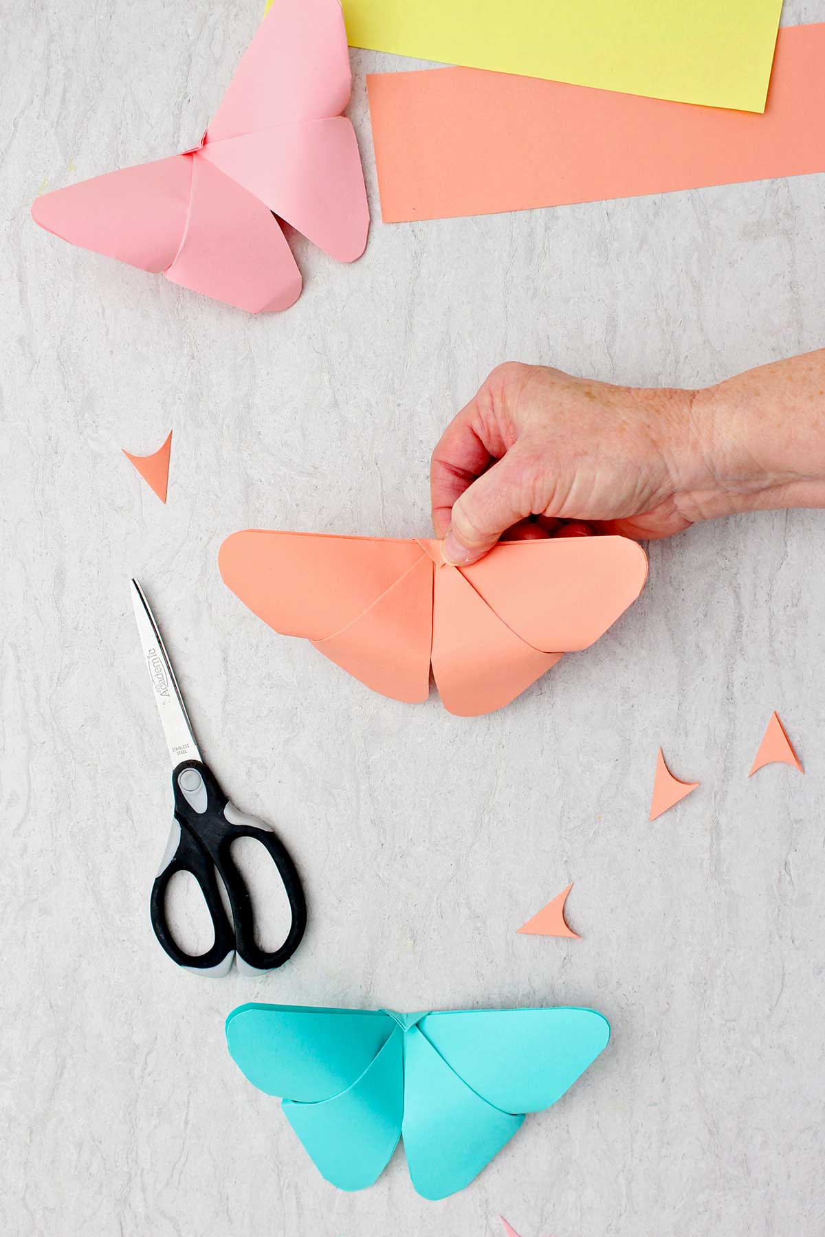 Uma pessoa mostrando o outro lado da ponta do triângulo dobrado em uma borboleta de origami finalizada.