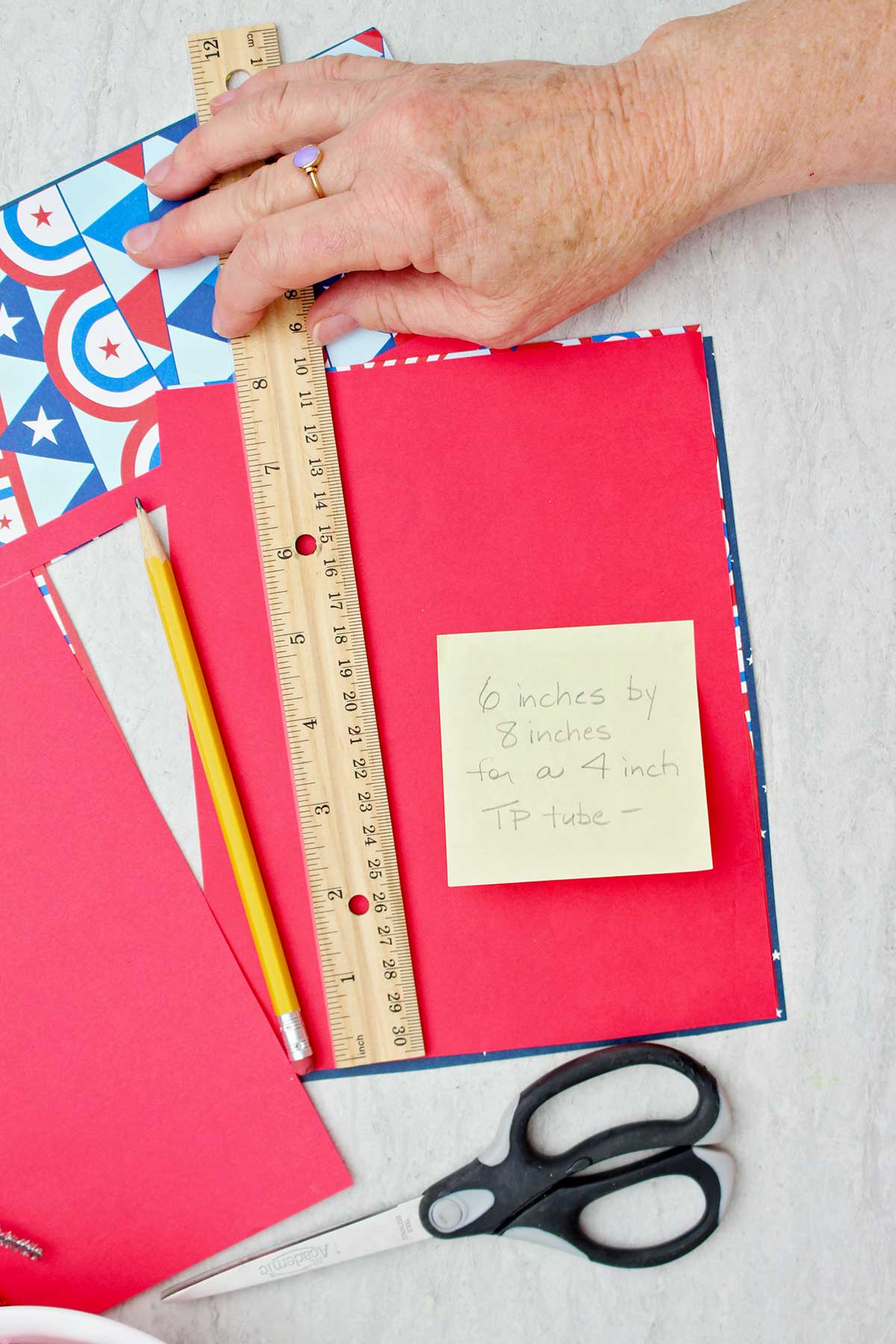 Pessoa medindo papel de scrapbooking para caber em torno de um tubo de papel toalha.