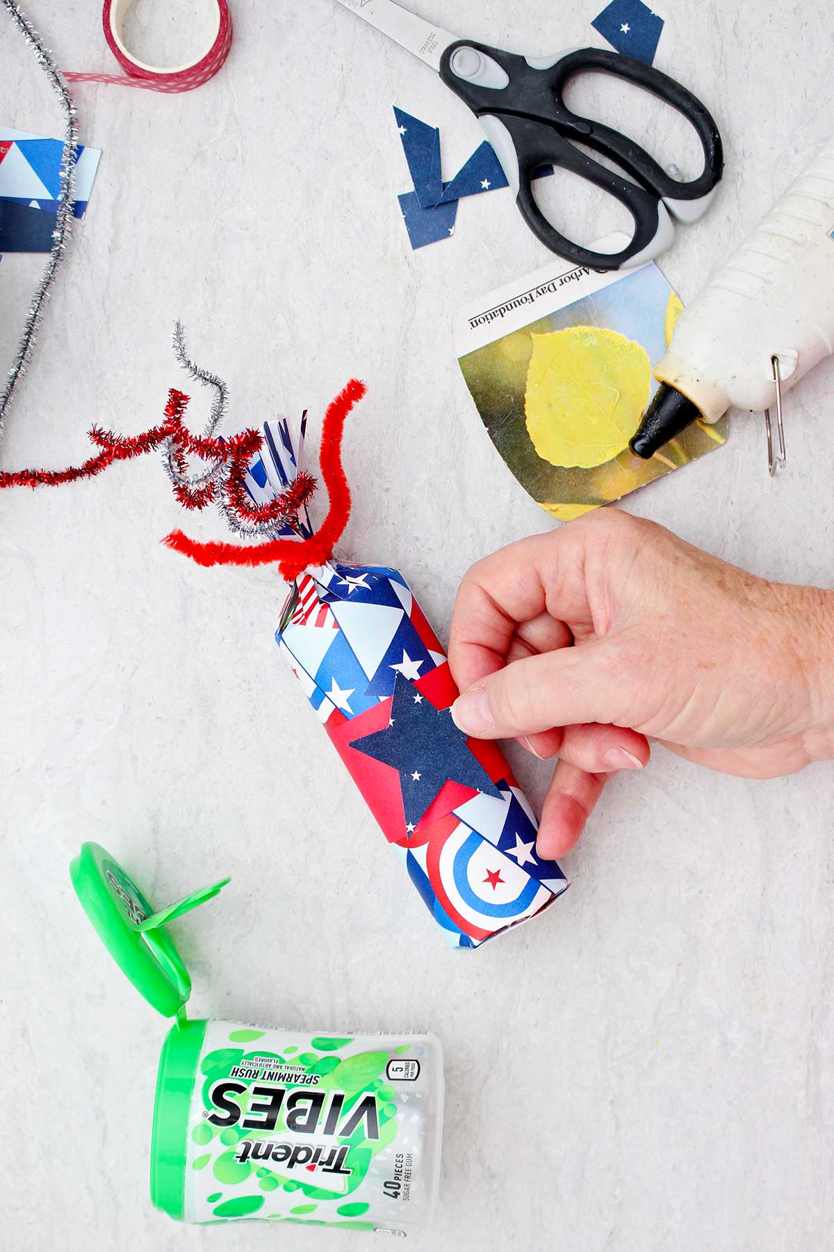 Pessoa colocando um pedaço de papel de scrapbook azul em forma de estrela em uma caixa de guloseima finalizada do 4 de Julho.