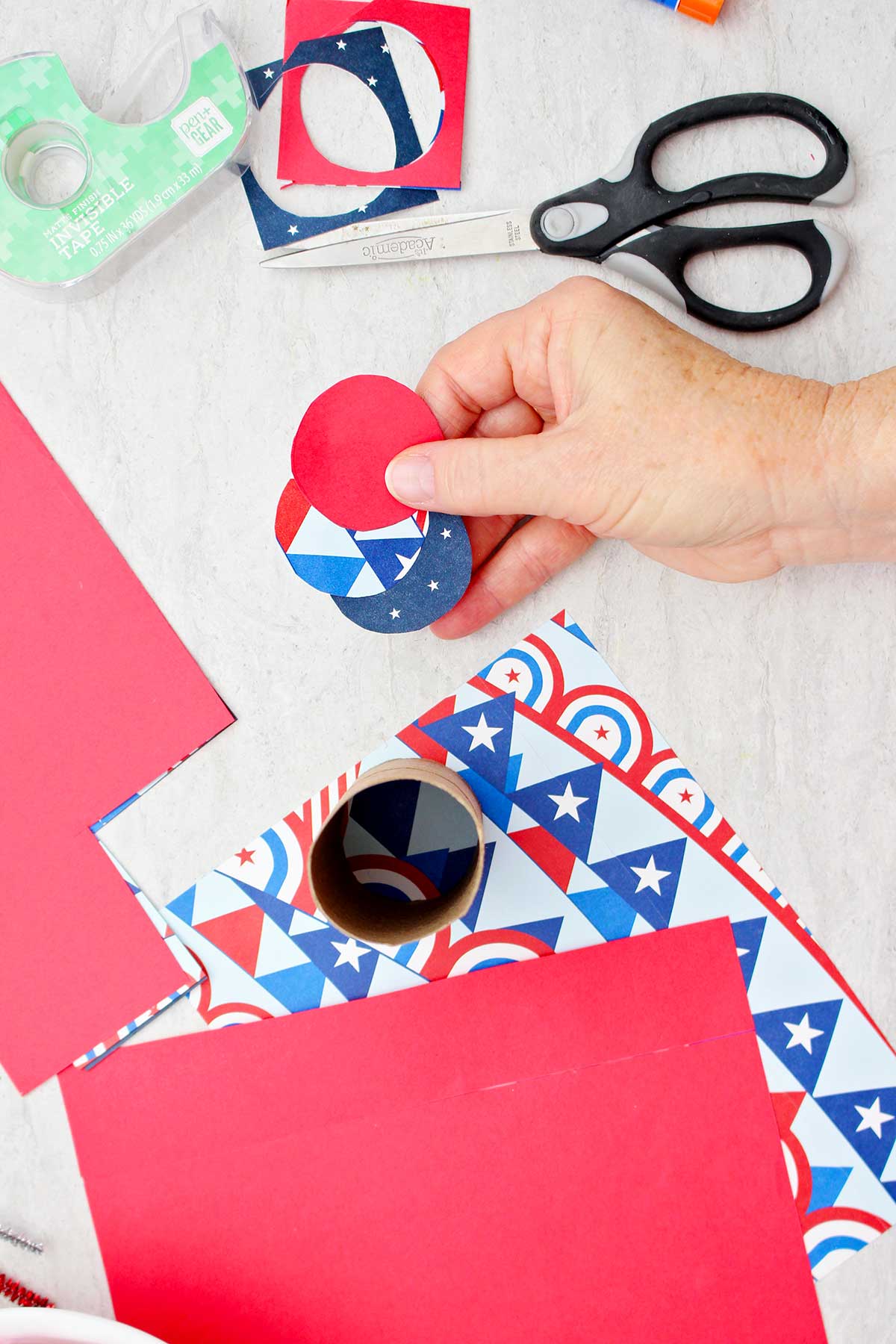 Pessoa segurando três recortes circulares de papel de scrapbook que serão usados para fechar a extremidade inferior de uma caixa de guloseimas em forma de foguete.