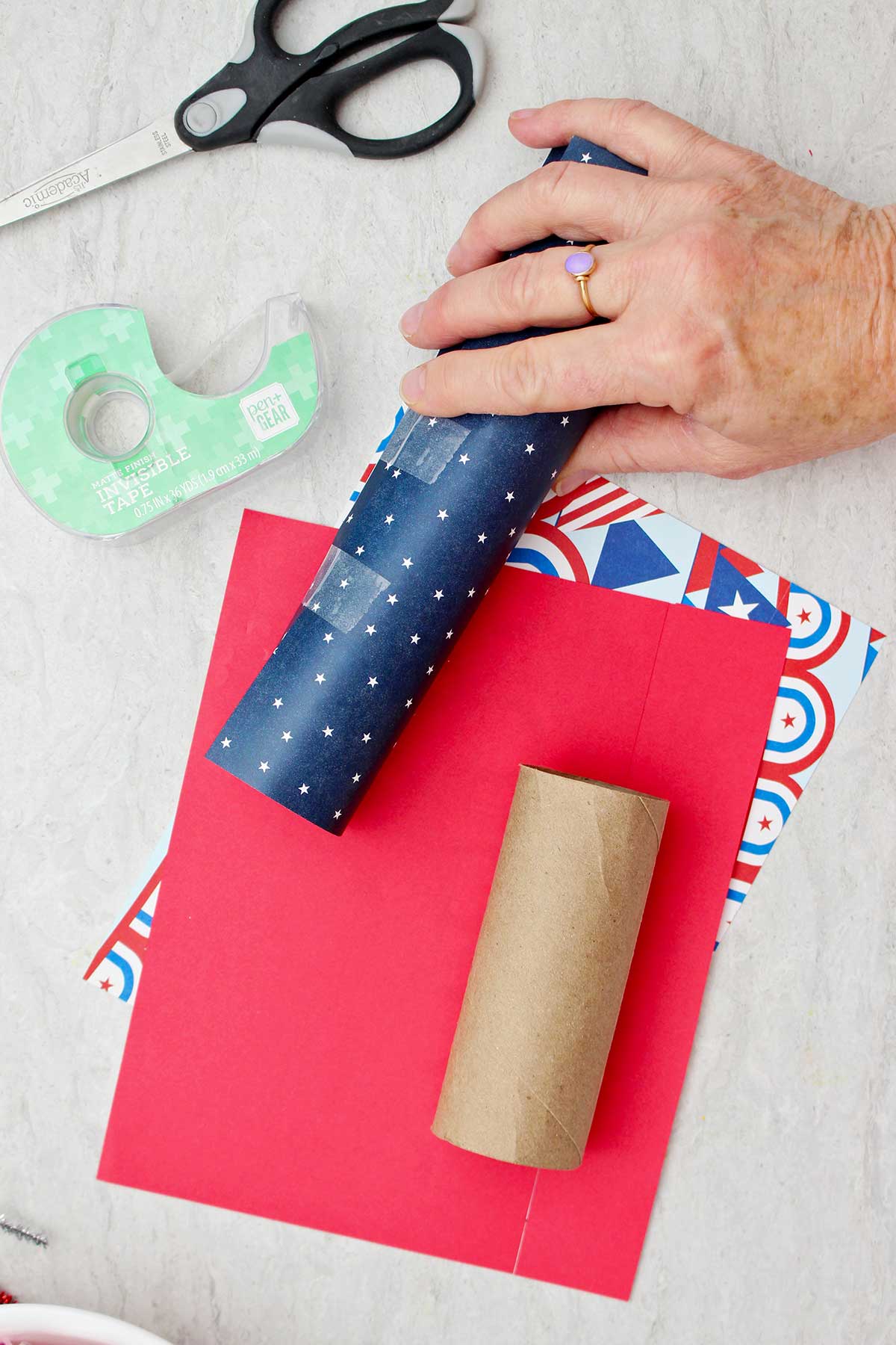 Pessoa segurando um tubo de papel higiênico enrolado em papel de scrapbook com padrão de estrelas azuis e colado.