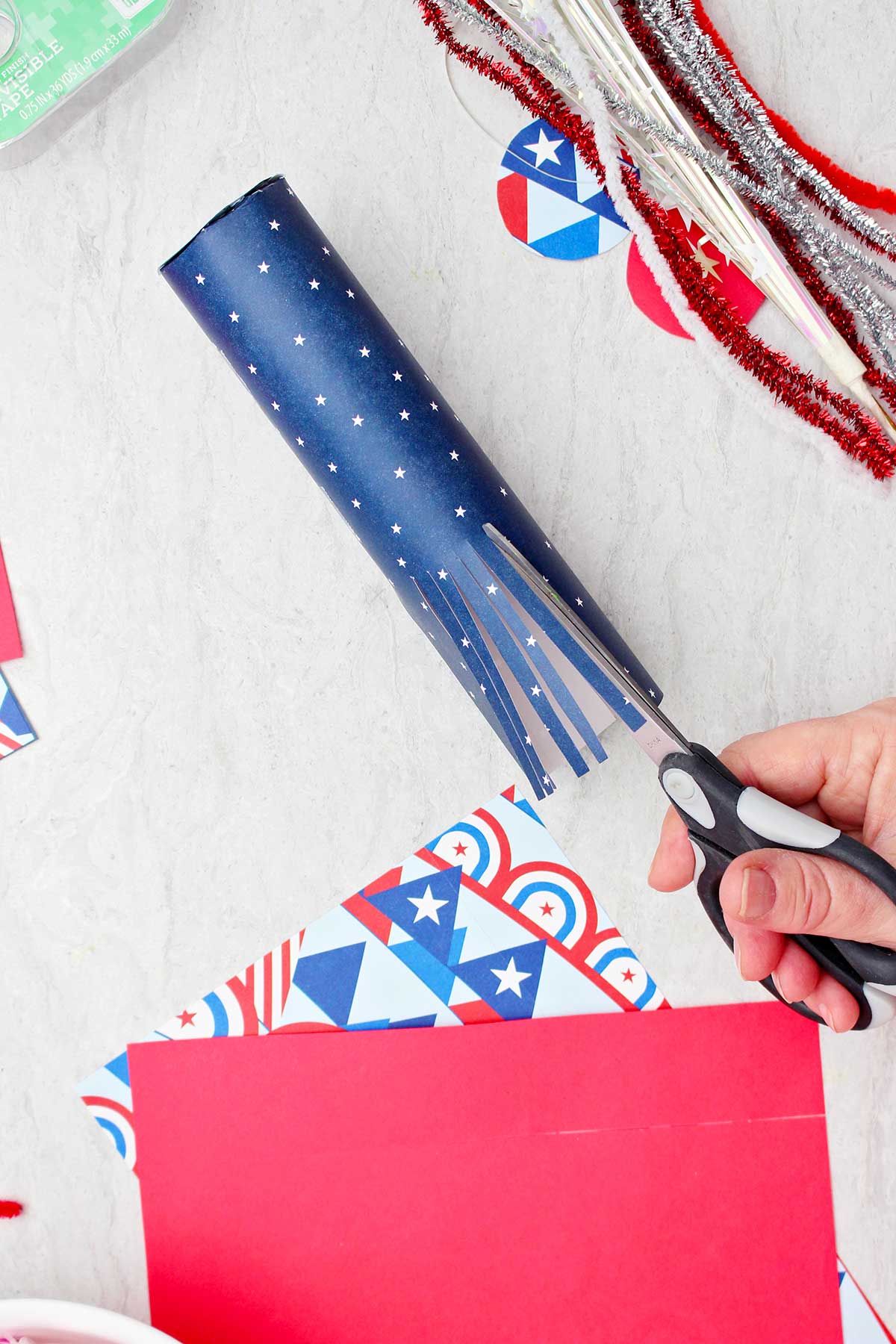 Pessoa cortando papel de scrapbook enrolado em um tubo de papel higiênico para parecer franjas.