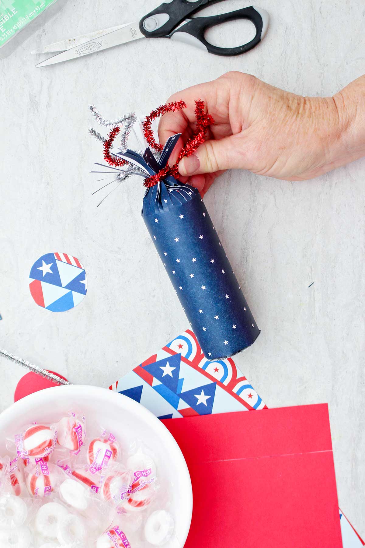 Pessoa enrolando um limpador de pipas vermelho brilhante no topo da caixa de guloseima em forma de foguete com padrão de estrela azul.