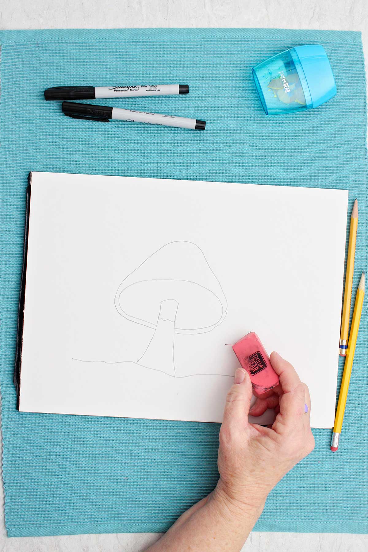 Um artista apagando linhas de um desenho de cogumelo em um pedaço de papel