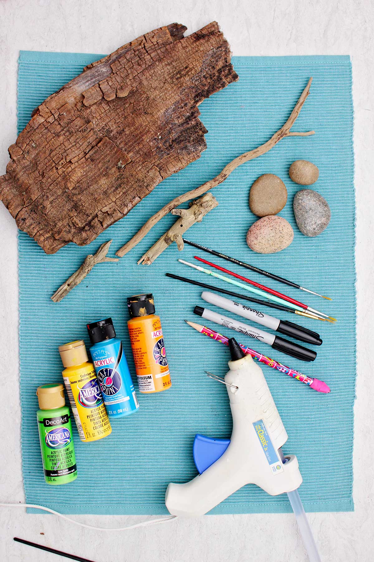 Pedras lisas, pincéis, marcadores sharpie, tinta, pistola de cola e pedaços de madeira para fazer arte em pedras pintadas de coruja.