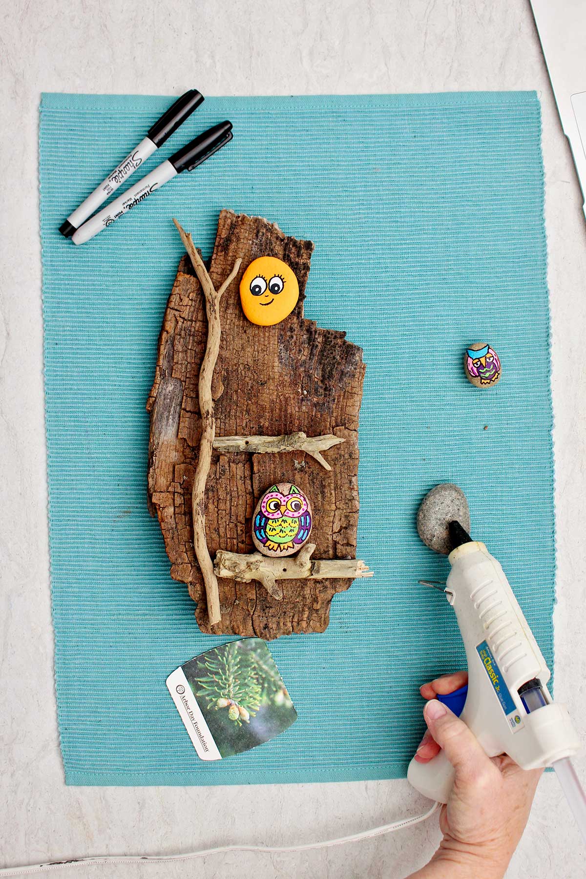 Pessoa colando a parte de trás de uma pedra pintada em uma peça de madeira.