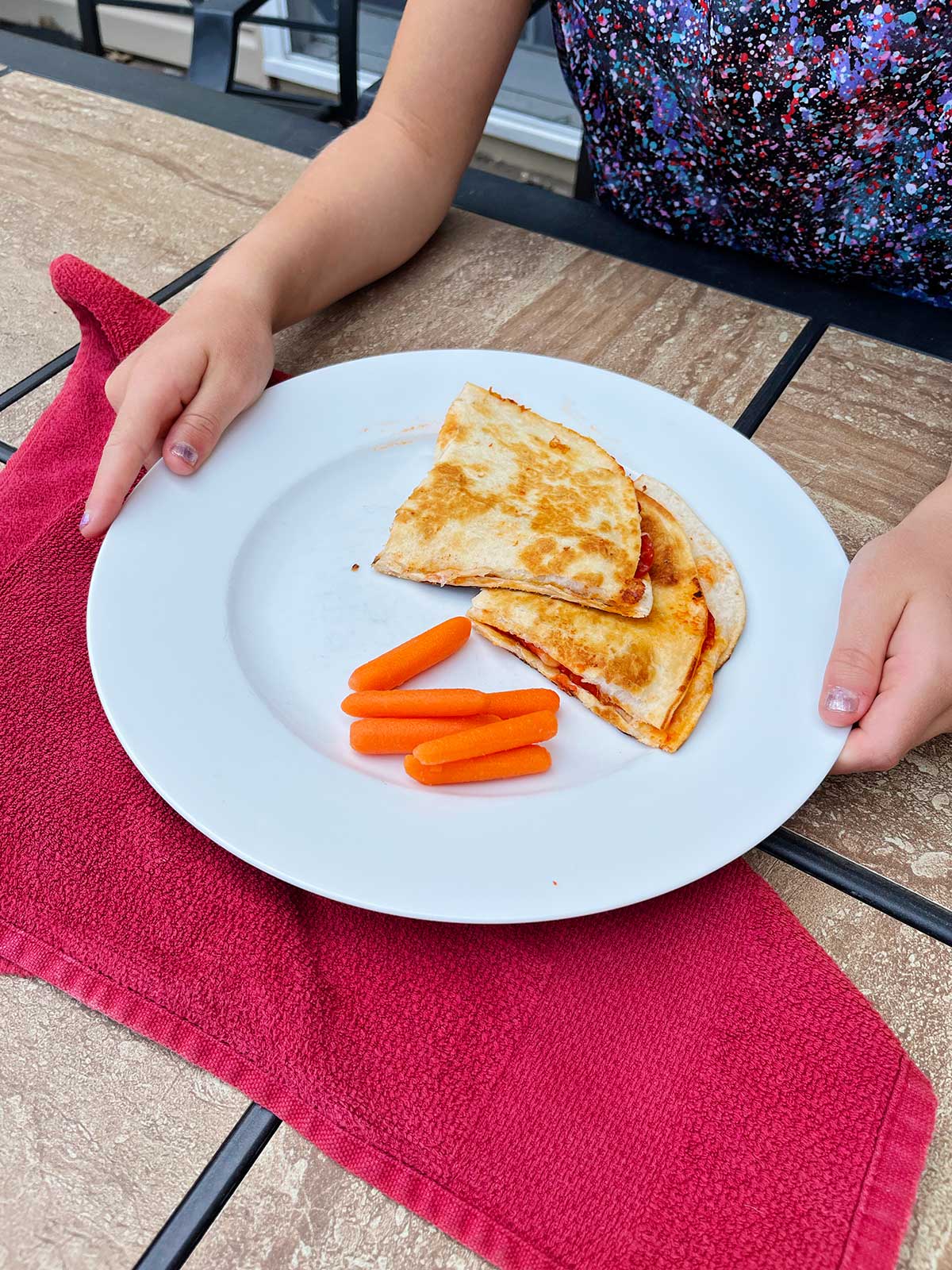 Duas quesadillas de pizza e cenouras baby em um prato branco.