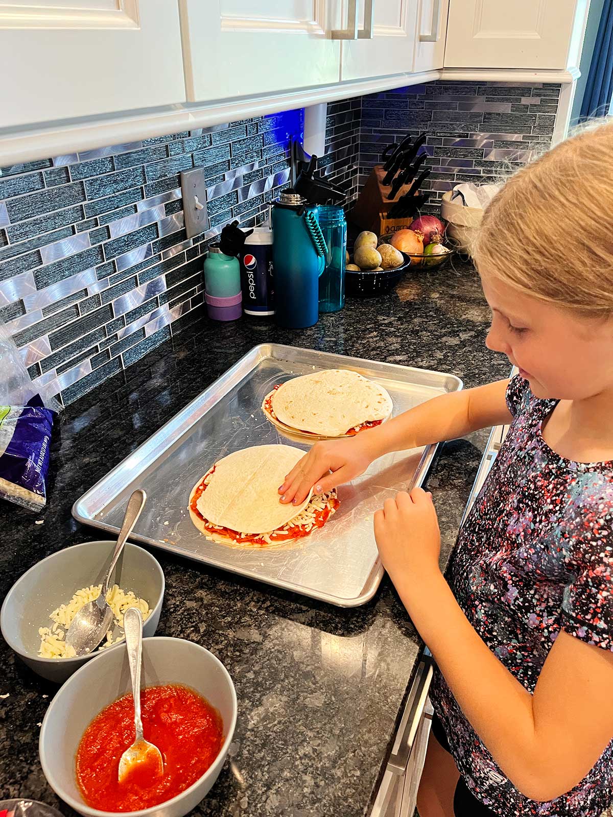 Uma menina jovem montando duas quesadillas de pizza na bancada.