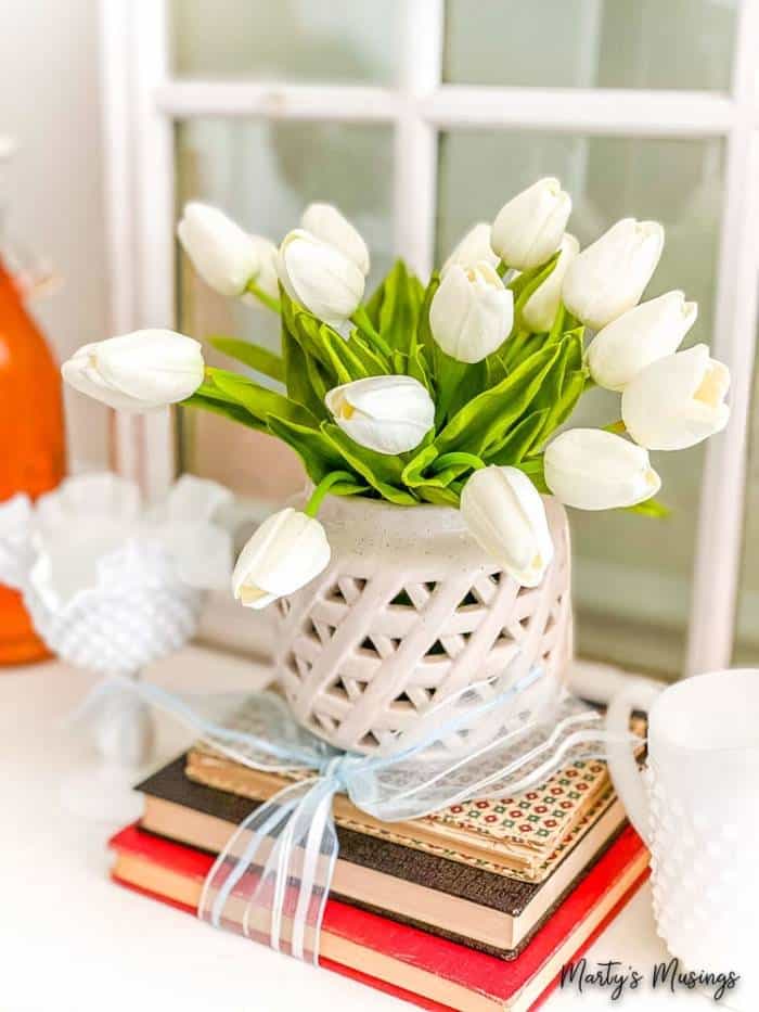 tulipas de seda branca empilhadas sobre livros amarrados com uma fita Um vaso de flores sobre uma mesa