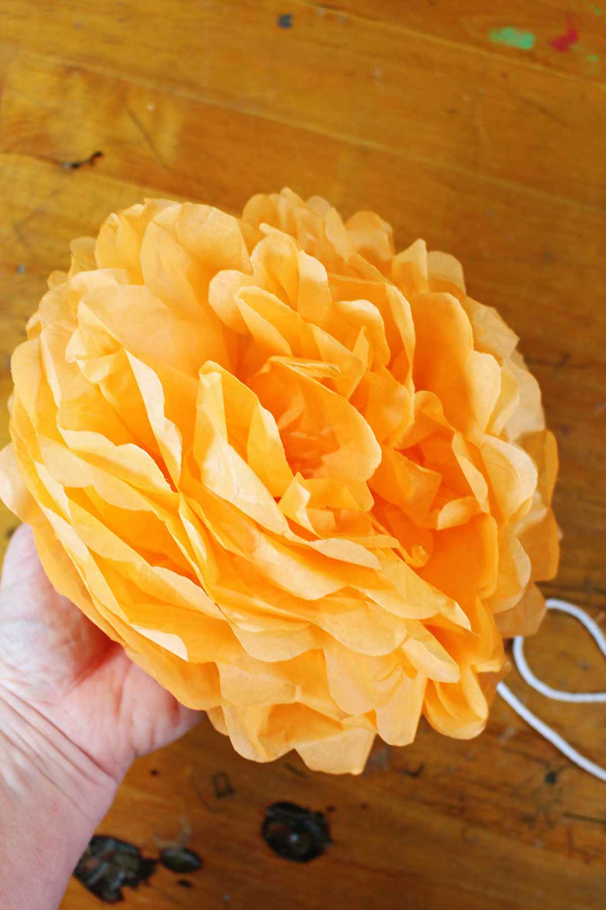 Mão segurando uma flor de papel de seda laranja concluída.