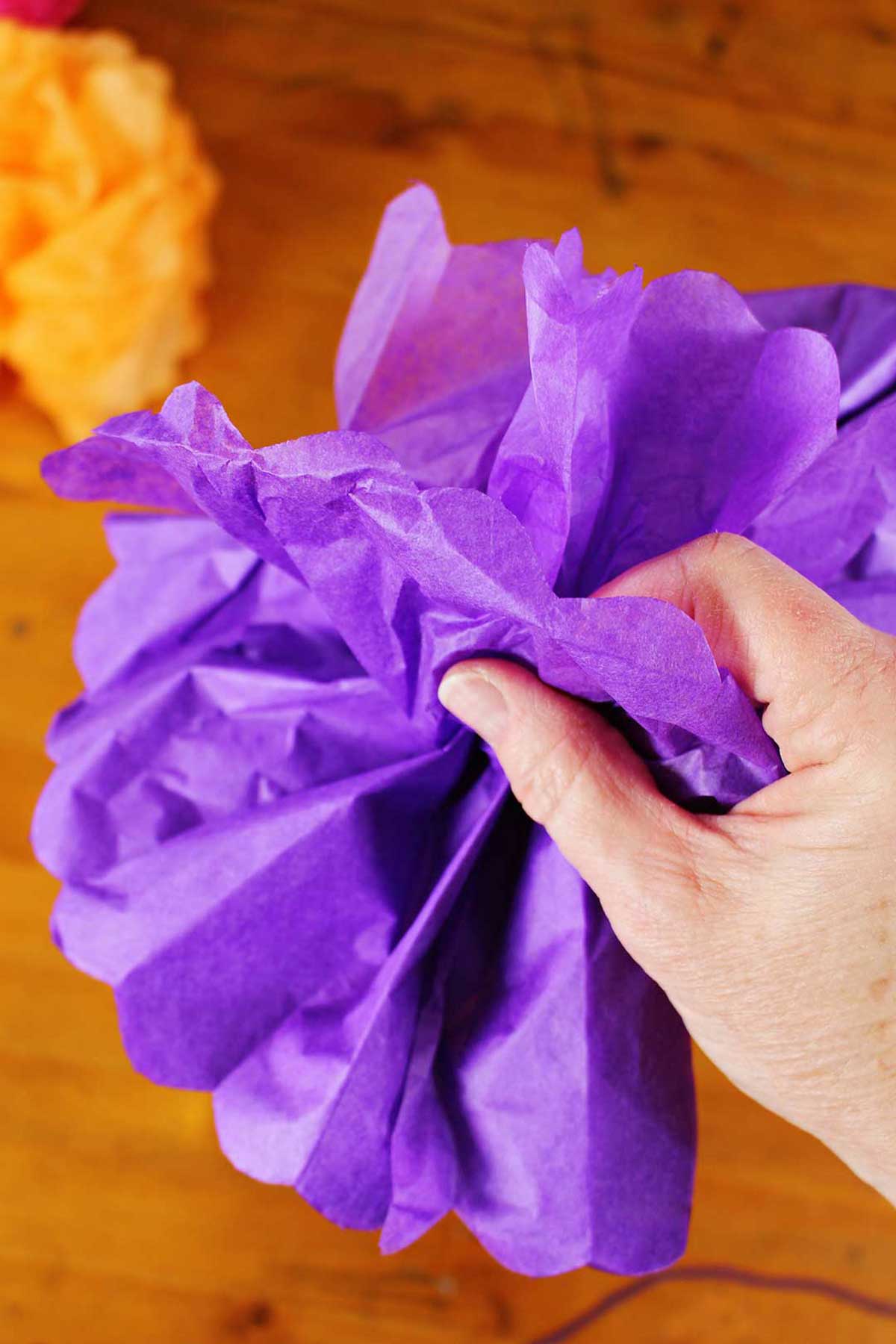 Mão abrindo e desgrenhando uma flor de papel de seda roxa.