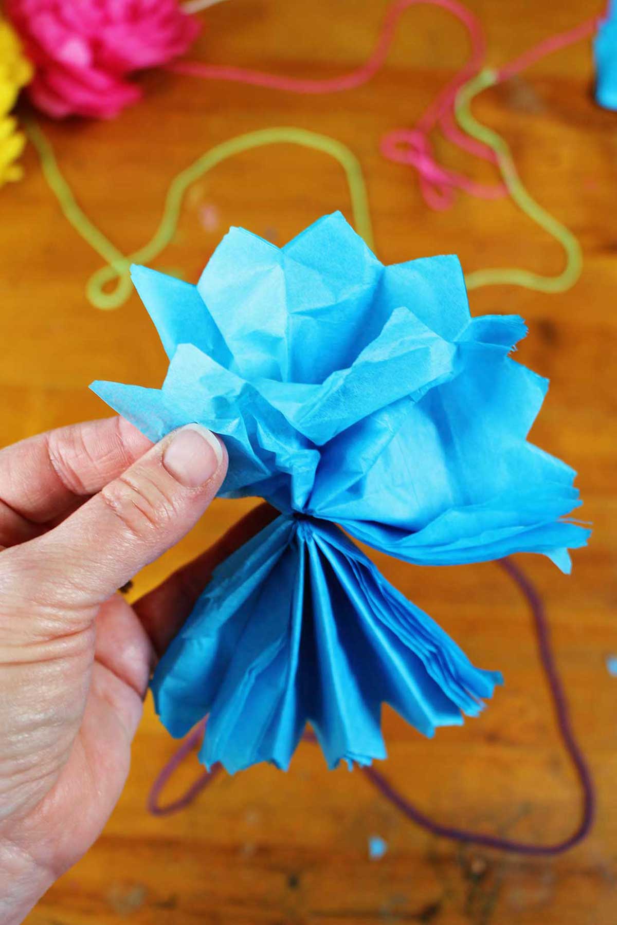 Mão abrindo e desgrenhando uma flor de papel de seda azul.