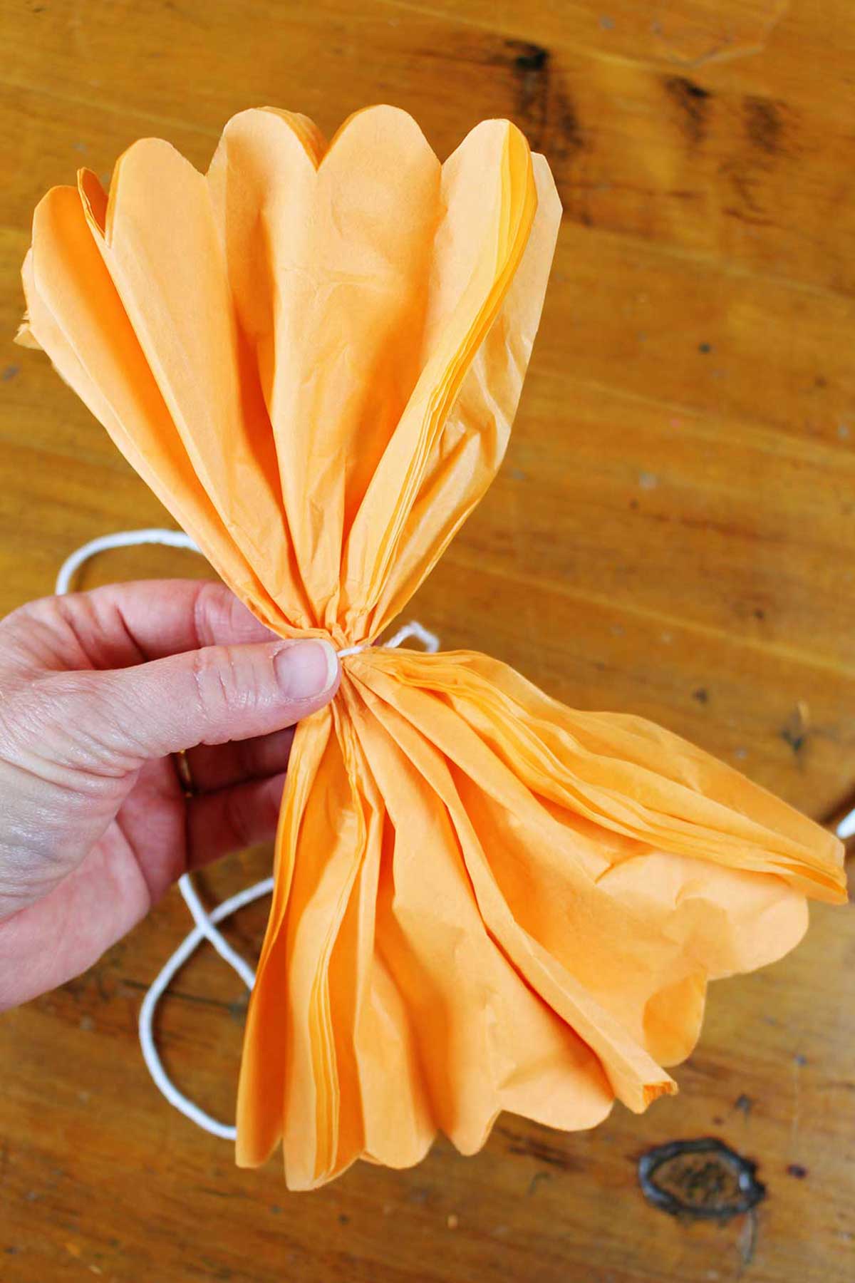 Mão segurando papel de seda laranja cortado e dobrado parcialmente aberto para mostrar a borda recortada.
