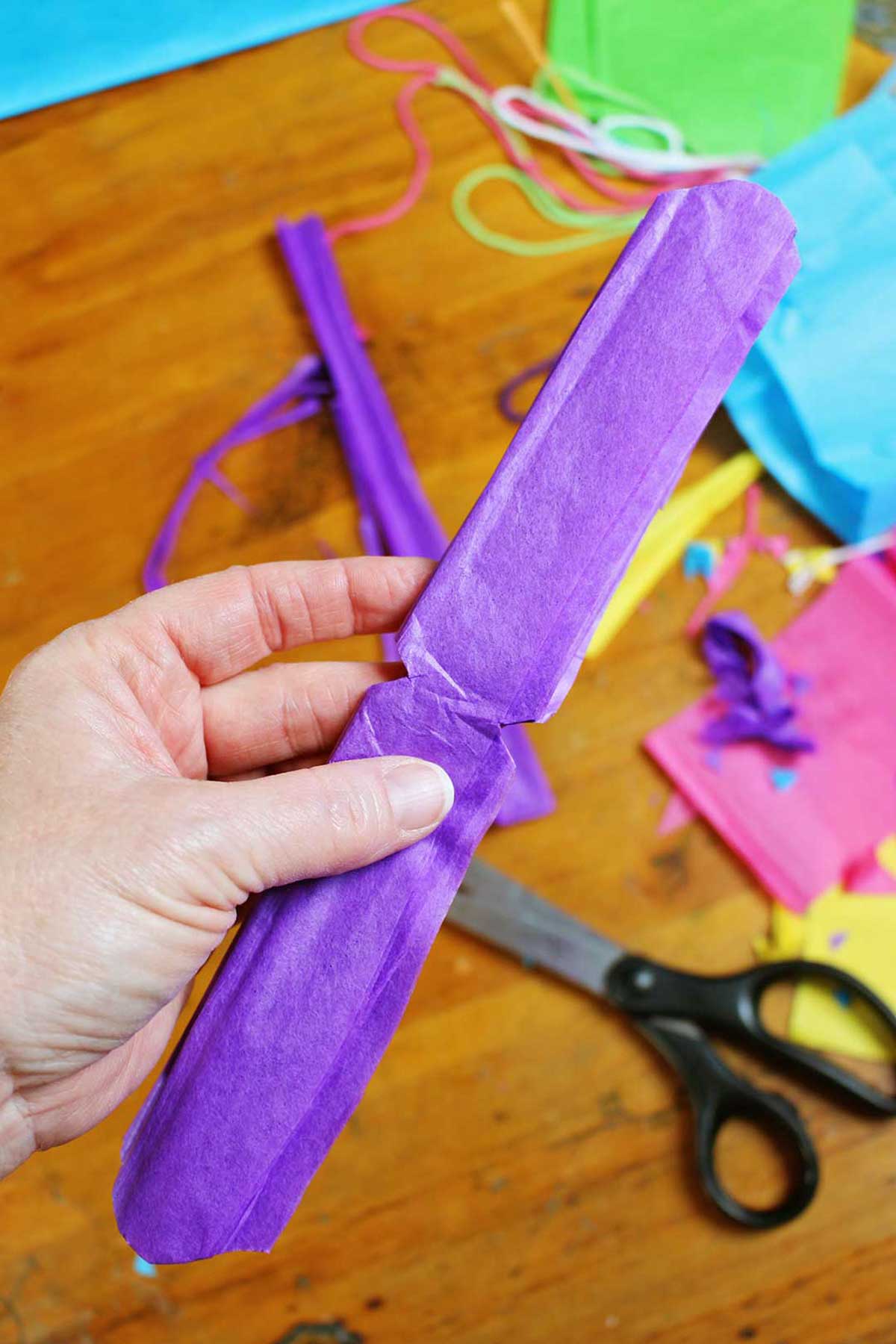 Mão segurando papel crepom roxo dobrado e aparado.