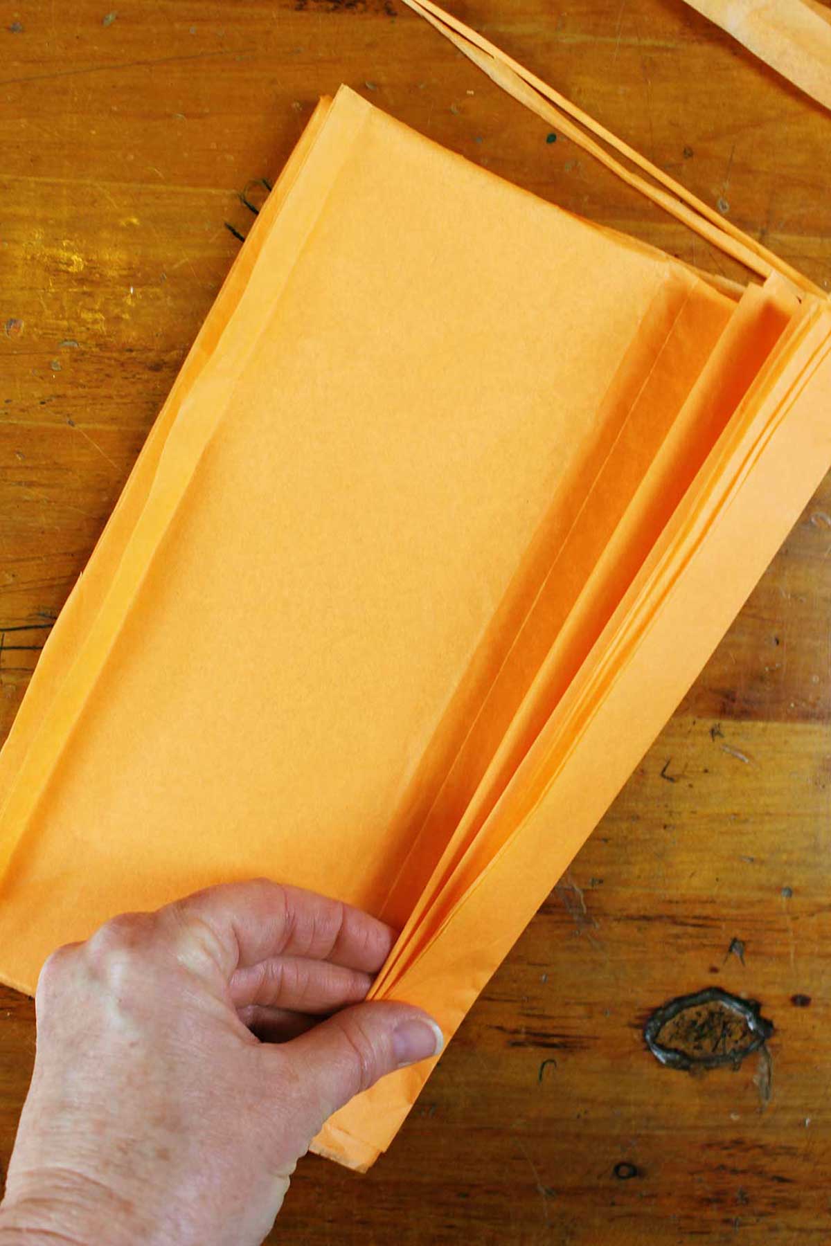 Mão dobrando uma pilha de papel de seda laranja.