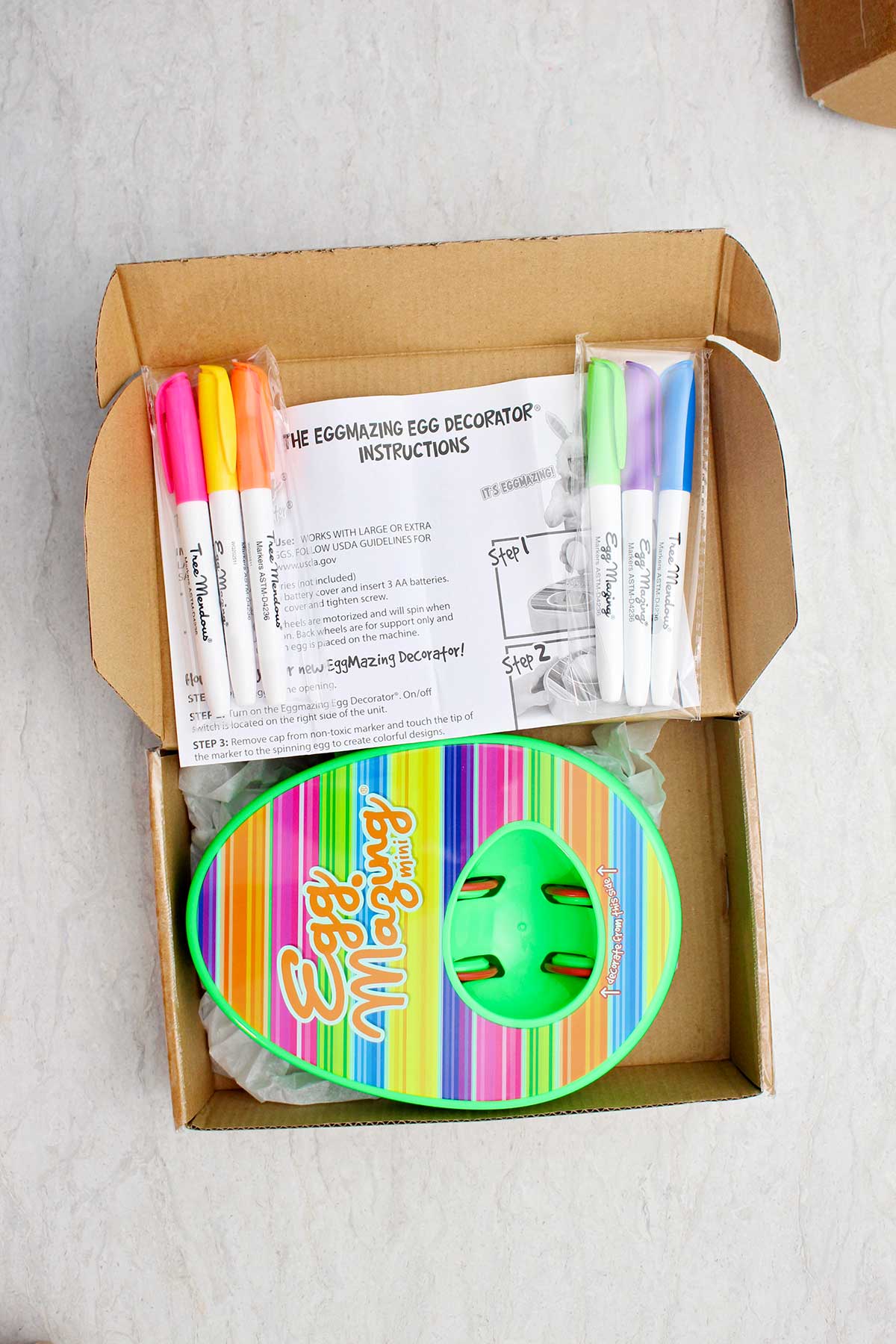 Uma caixa cheia de um kit EggMazing, marcadores e instruções.