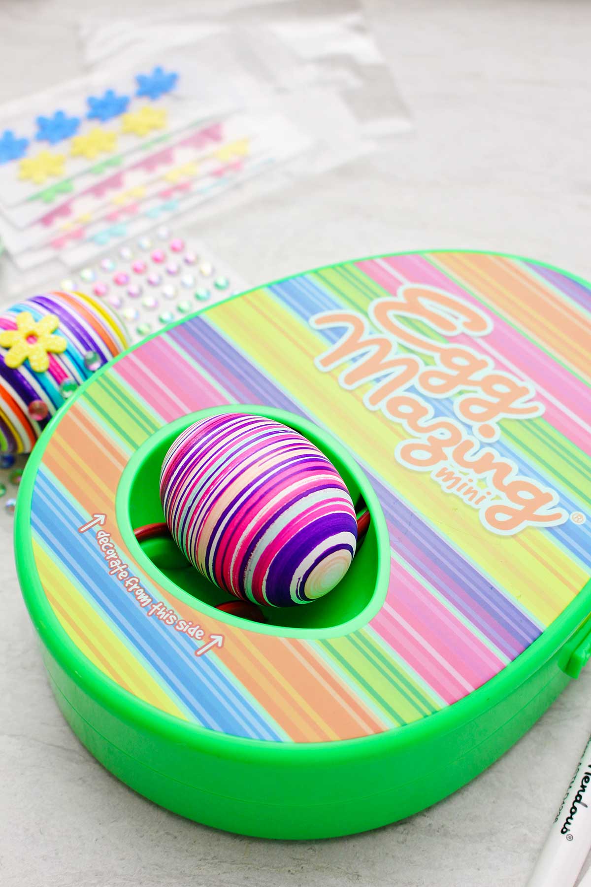 Kit de design com listras do EggMazing com ovo colorido listrado dentro e outros materiais por perto.
