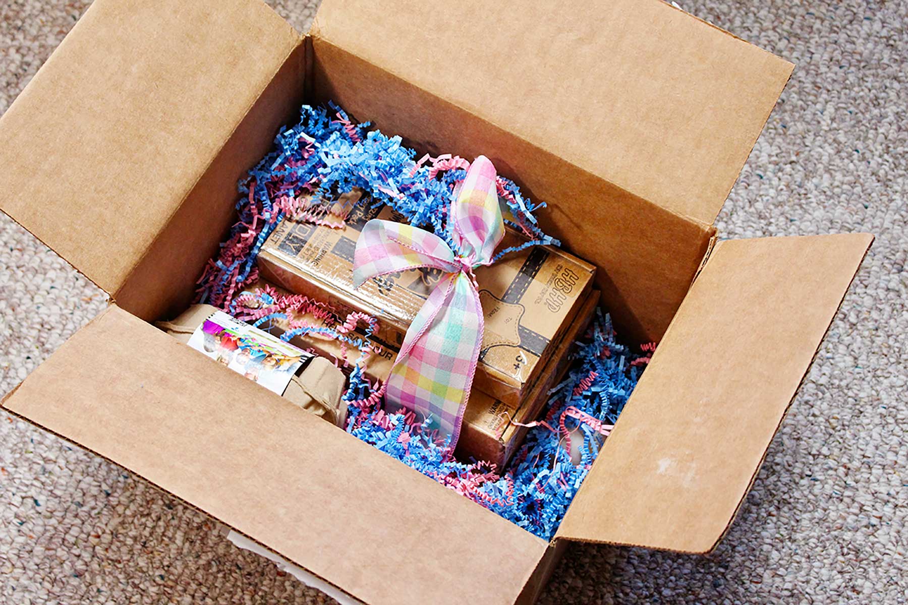Uma caixa cheia de um presente de kits EggMazing, ovos de madeira e grama de Páscoa.