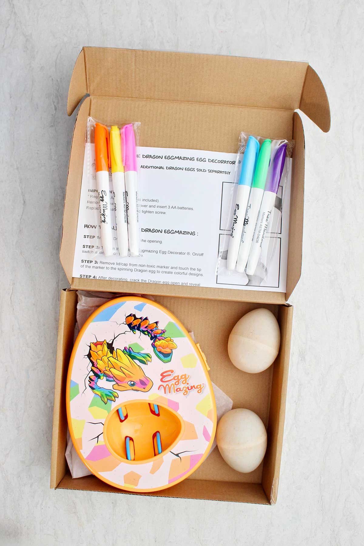 Uma caixa cheia de um kit EggMazing, marcadores, instruções e ovos de madeira.