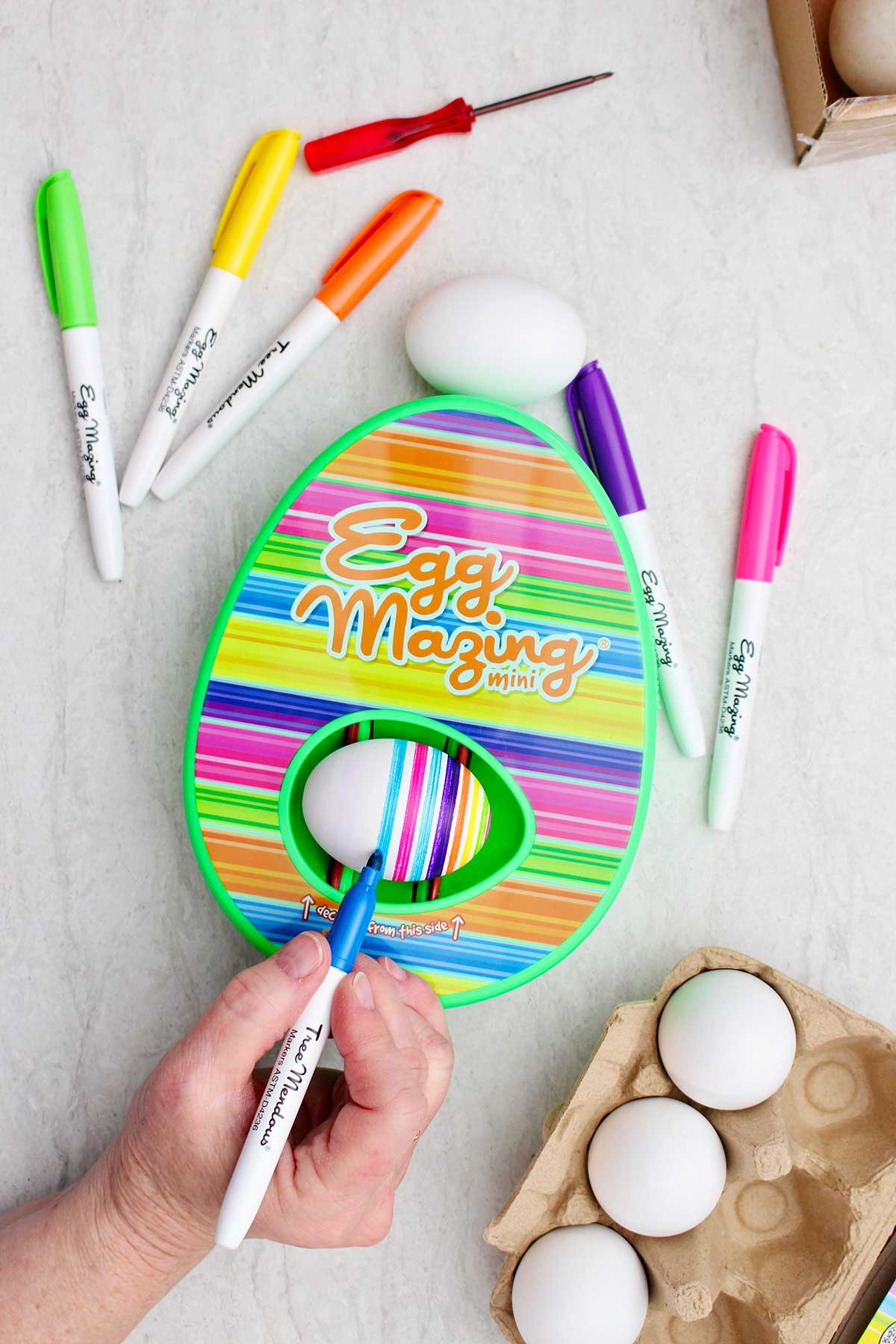 Uma pessoa usando um marcador azul para fazer listras no ovo do kit EggMazing.