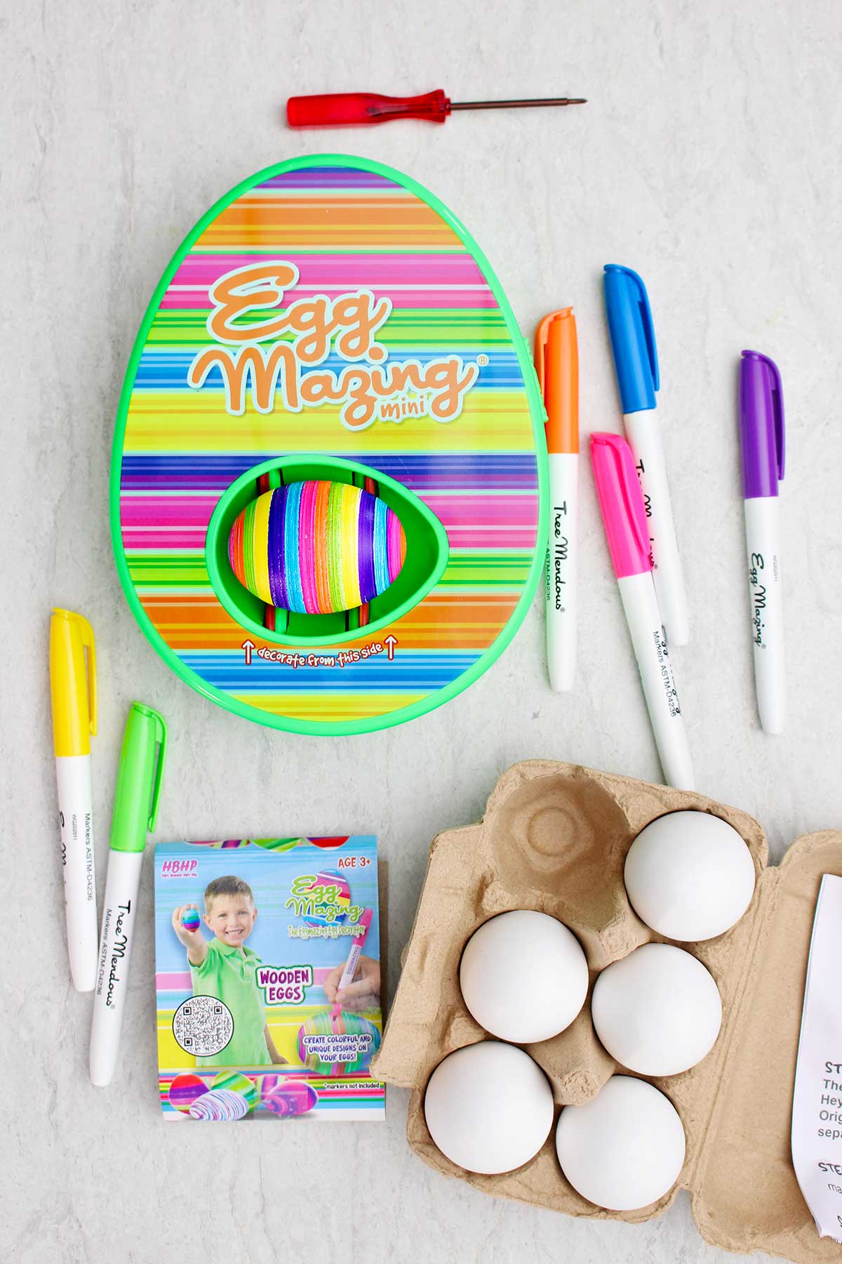 O kit listrado EggMazing completo com marcadores, ovos de madeira e ovos em uma cartela.
