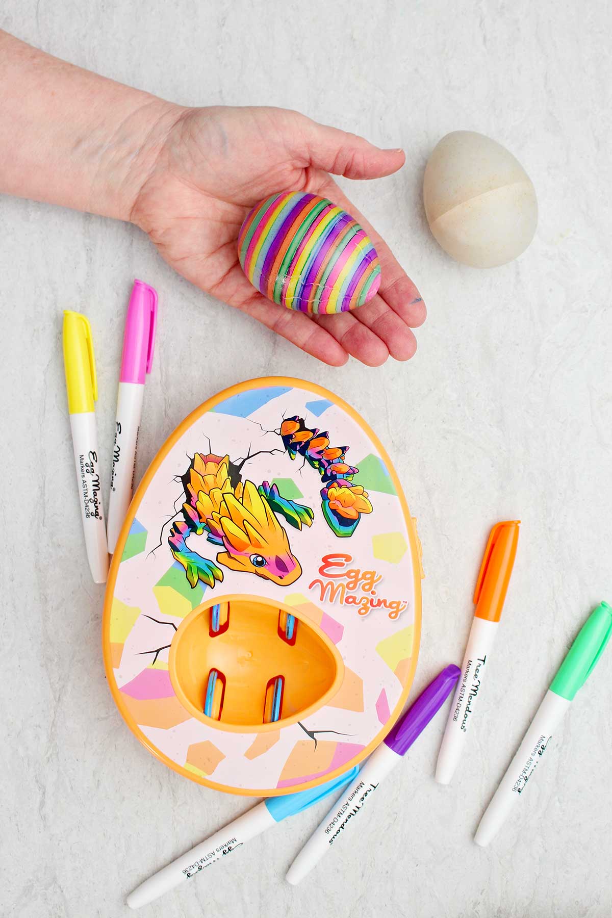 Uma pessoa segurando um ovo colorido listrado com o kit Dragão EggMazing ao lado.
