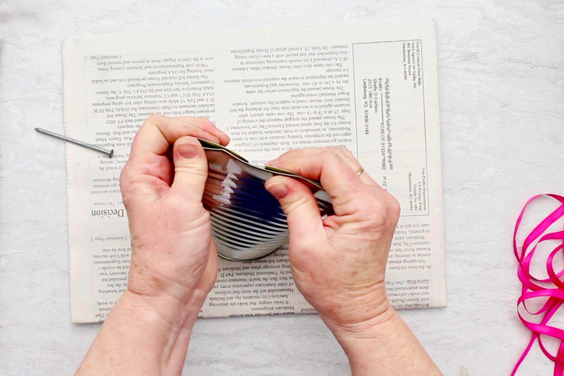 Uma pessoa achatando a parte inferior de uma lata sobre um pedaço de papel de jornal.
