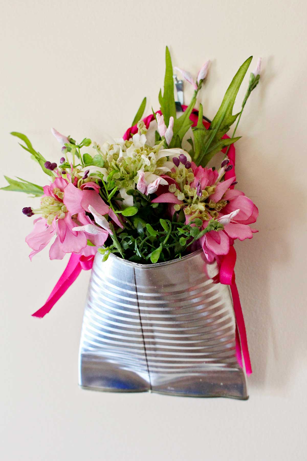 Um vaso de flores de lata reciclada preenchido com flores rosas e folhagens.