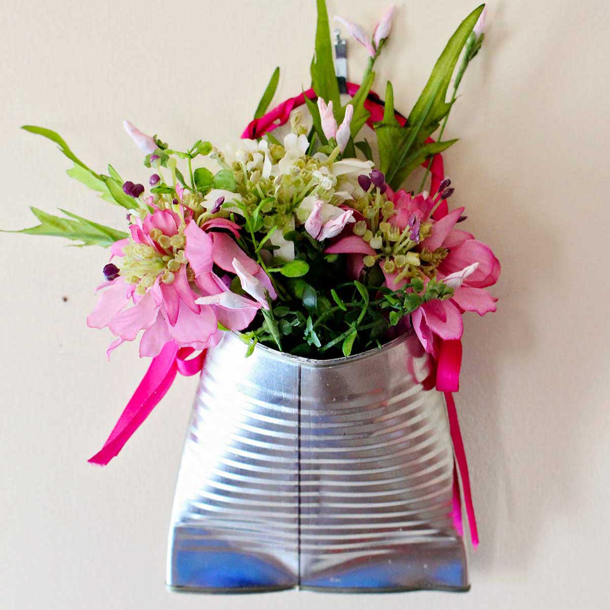 Um vaso de flores de lata reciclada completo, cheio de flores rosas e folhagens.