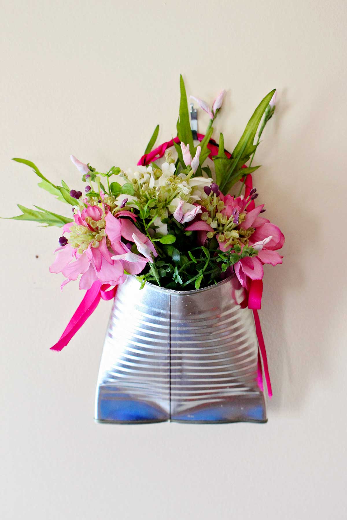 Um vaso de lata reciclado completo, cheio de flores rosas e folhagens.