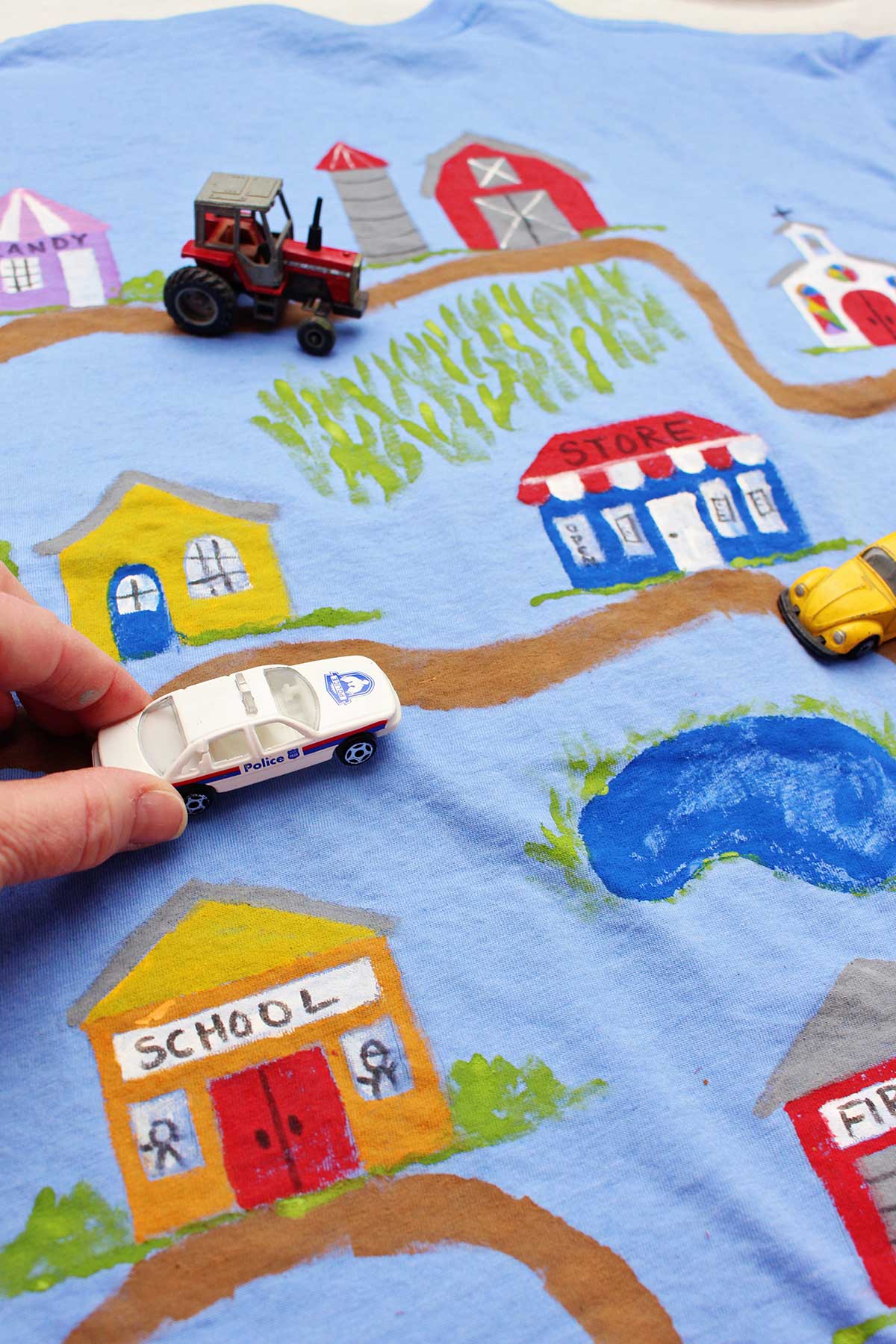 Uma pessoa dirigindo um carro de polícia em uma camiseta do Dia dos Pais completa, mostrando uma estrada de terra que leva a vários edifícios da cidade.