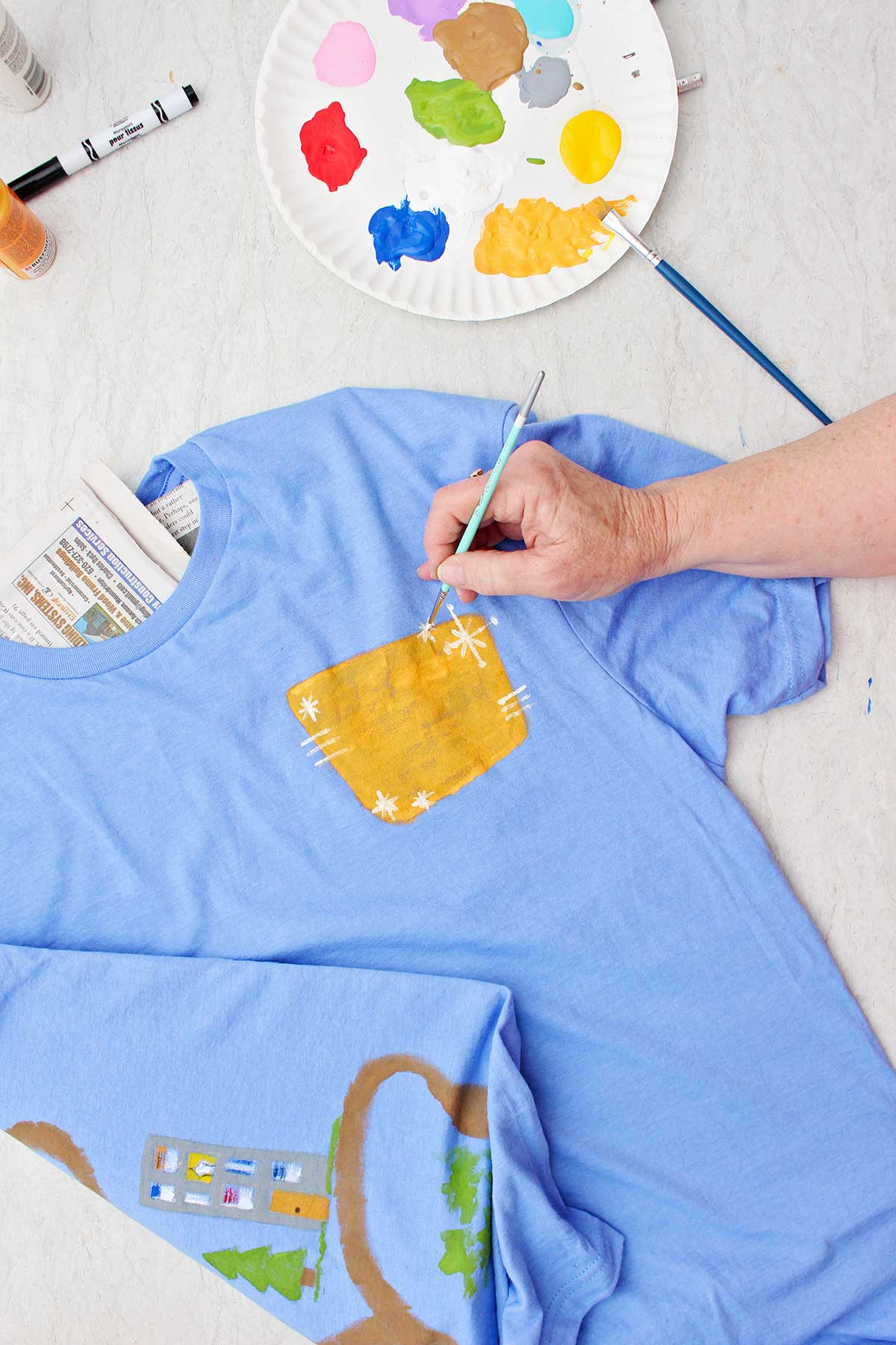 Uma pessoa pintando detalhes brancos em torno de uma placa amarela para a parte frontal da camiseta do Dia dos Pais.