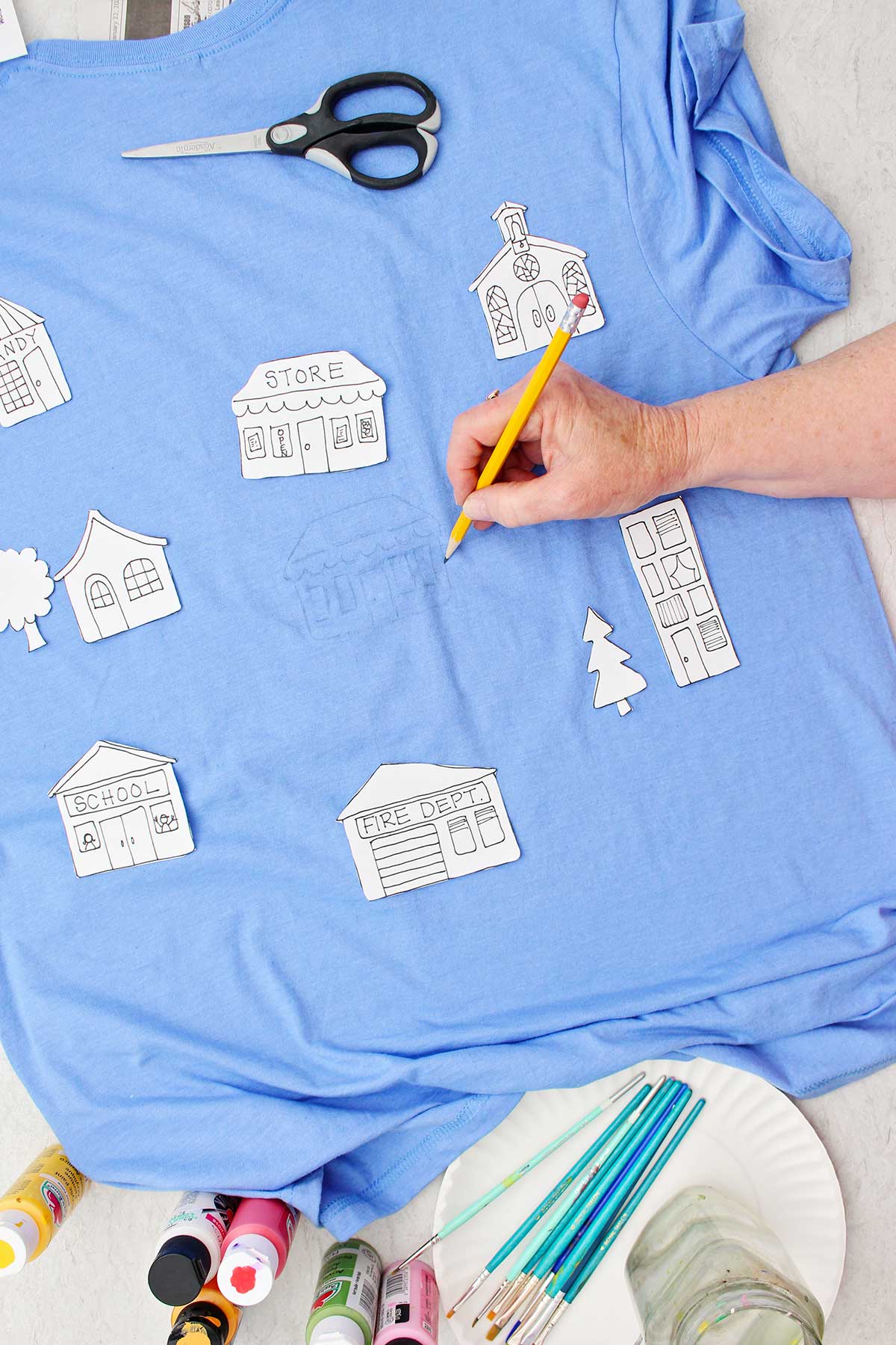 Uma pessoa desenhando detalhes em uma loja em uma camiseta azul com outros moldes de edifícios repousando sobre a camiseta.