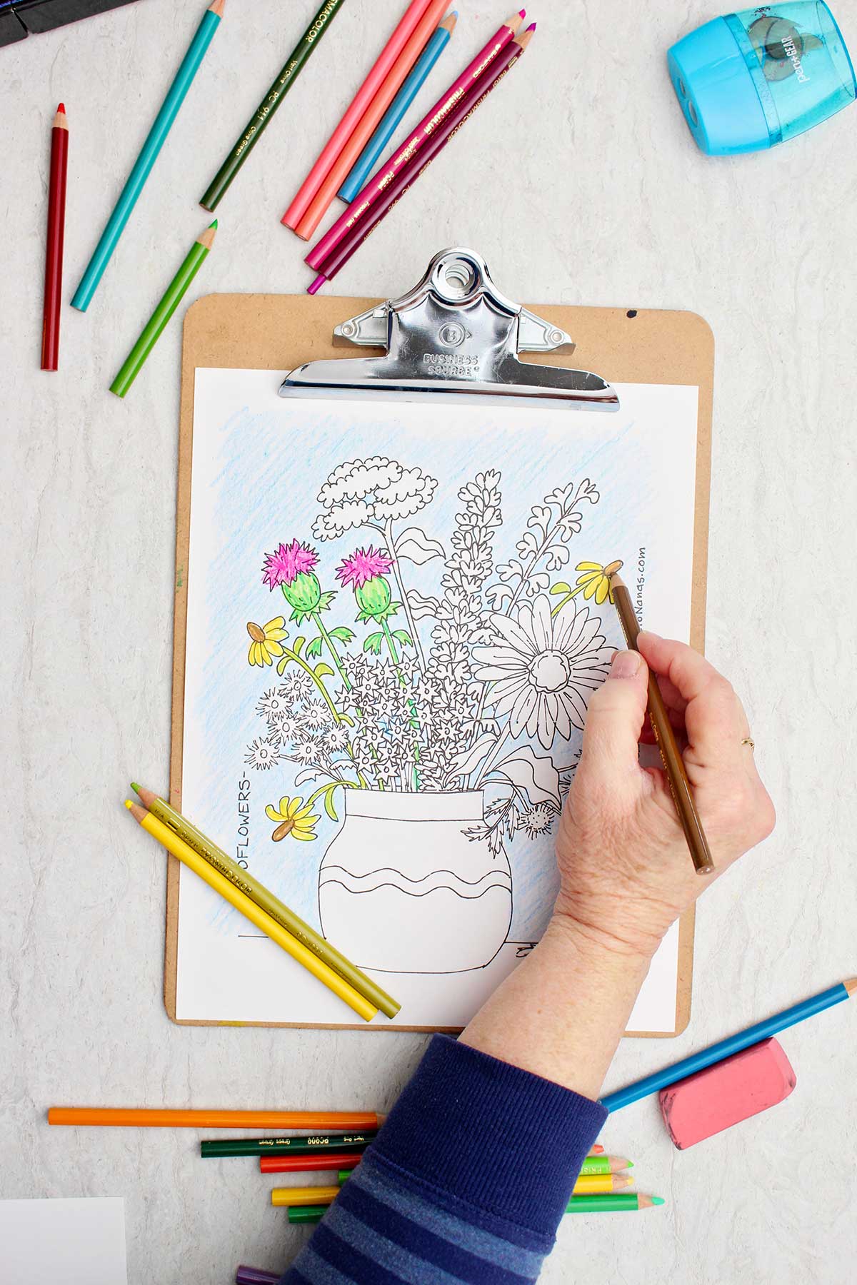 Pessoa colorindo uma margarida de amarelo na página de colorir de um buquê de flores silvestres em um vaso.