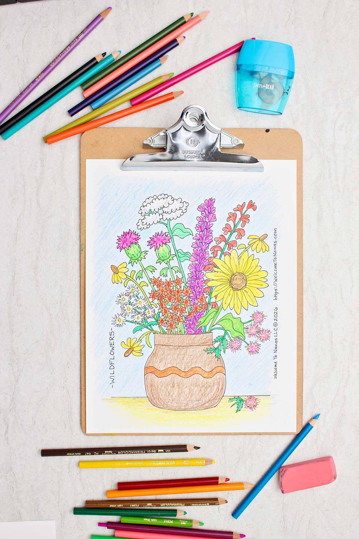 Uma página de colorir de um vaso marrom cheio de flores silvestres coloridas preso a uma prancheta com lápis de cor espalhados ao redor.