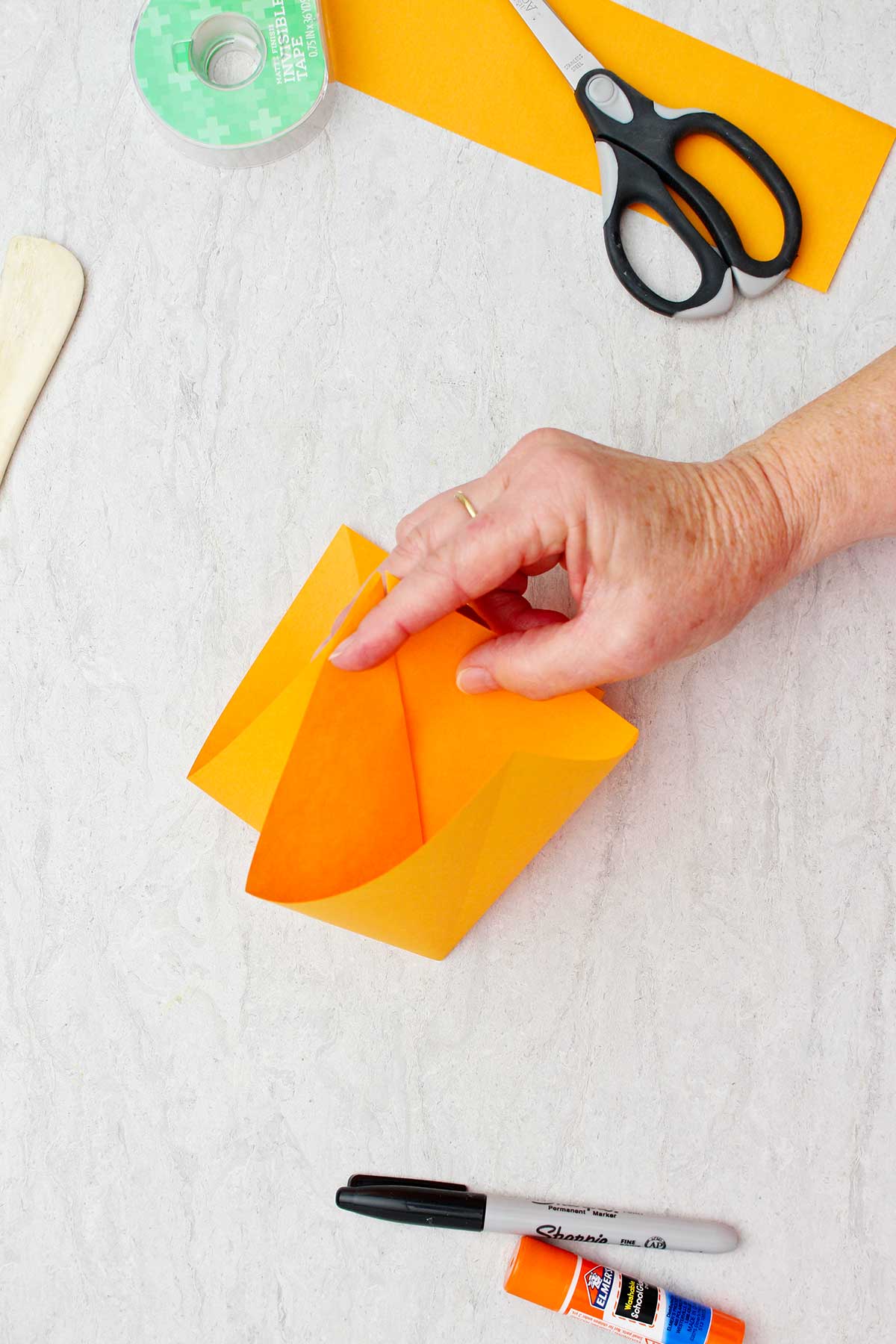 Pessoa mostrando a visão interna do papel laranja dobrado para fazer uma abóbora de origami.