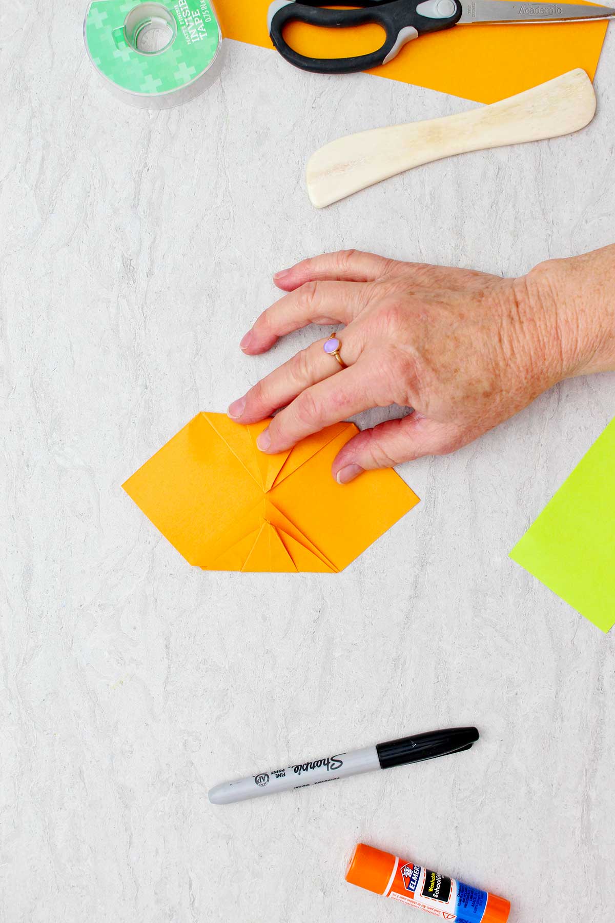 Pessoa dobrando dois lados dobrados em direção um ao outro para criar uma abóbora de origami.