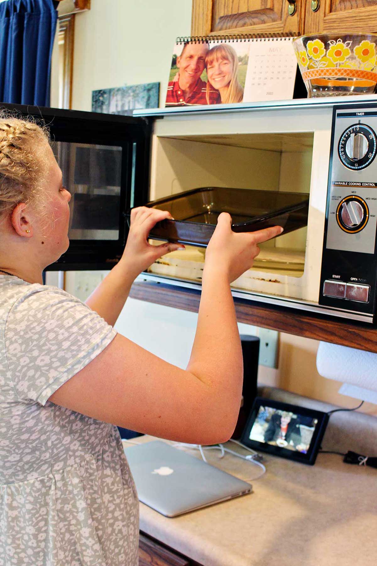 Uma menina colocando uma panela de vidro no micro-ondas.