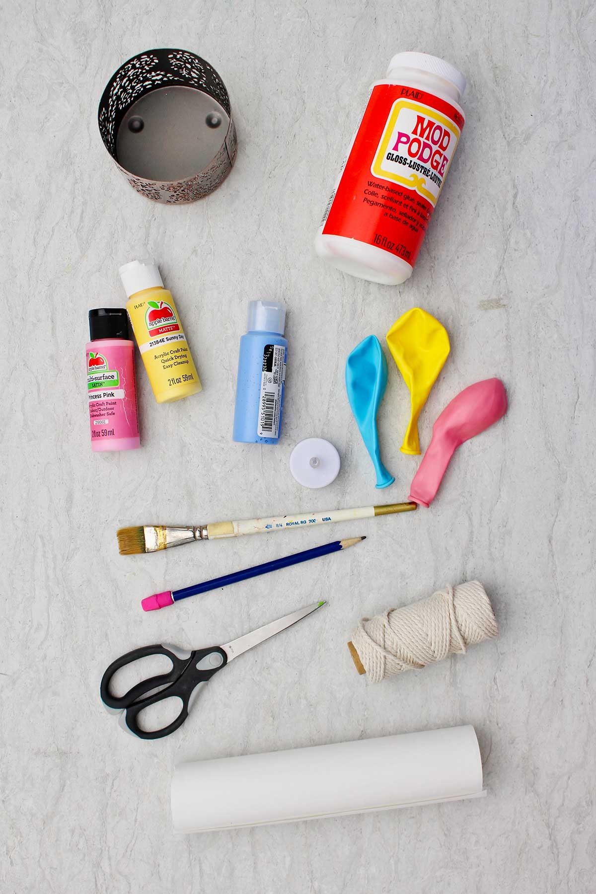Materiais usados para fazer um mini balão de ar quente. Modge lodge, corda, balões, pincel, toalhas de papel, tinta, tesoura e uma cesta de metal.