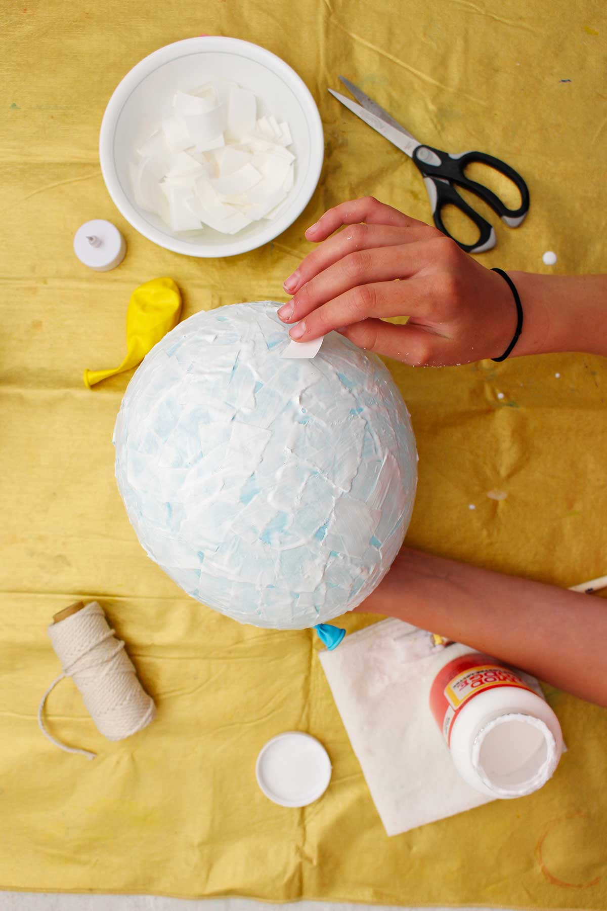 Pessoa colocando pedaços de papel machê em um balão azul.