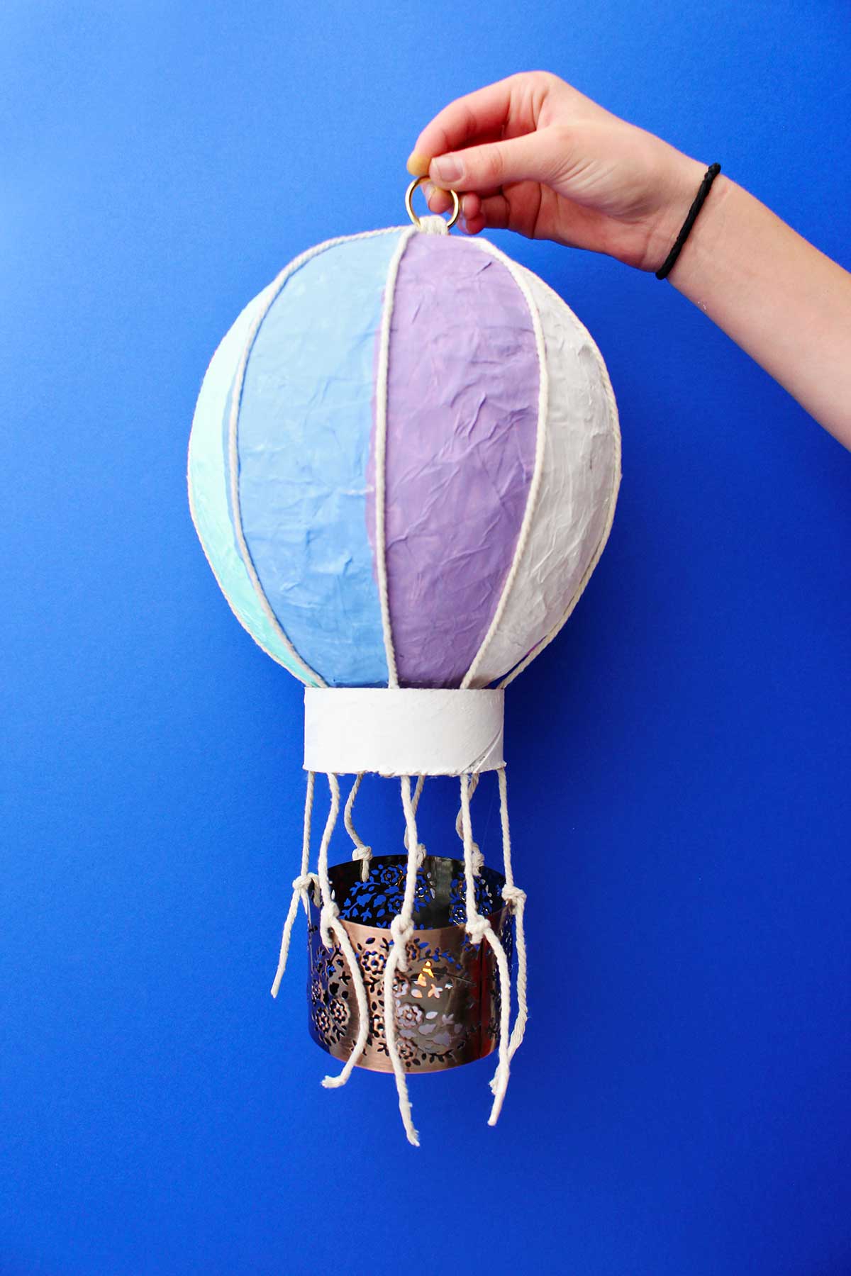 Pessoa segurando um artesanato de mini balão de ar quente completo contra um fundo azul.