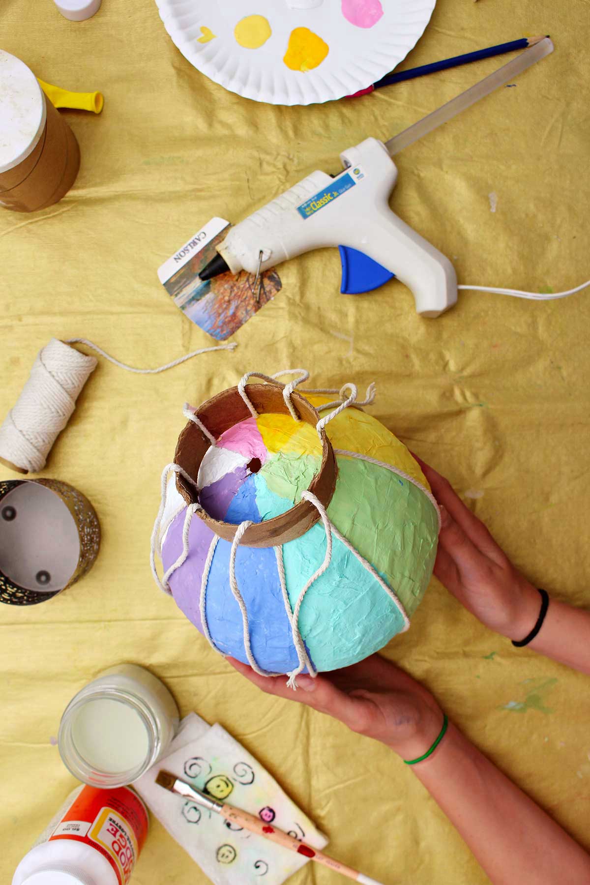 Pessoa mostrando a parte inferior de um mini balão de ar quente com cordas prontas para serem presas a uma cesta de metal.
