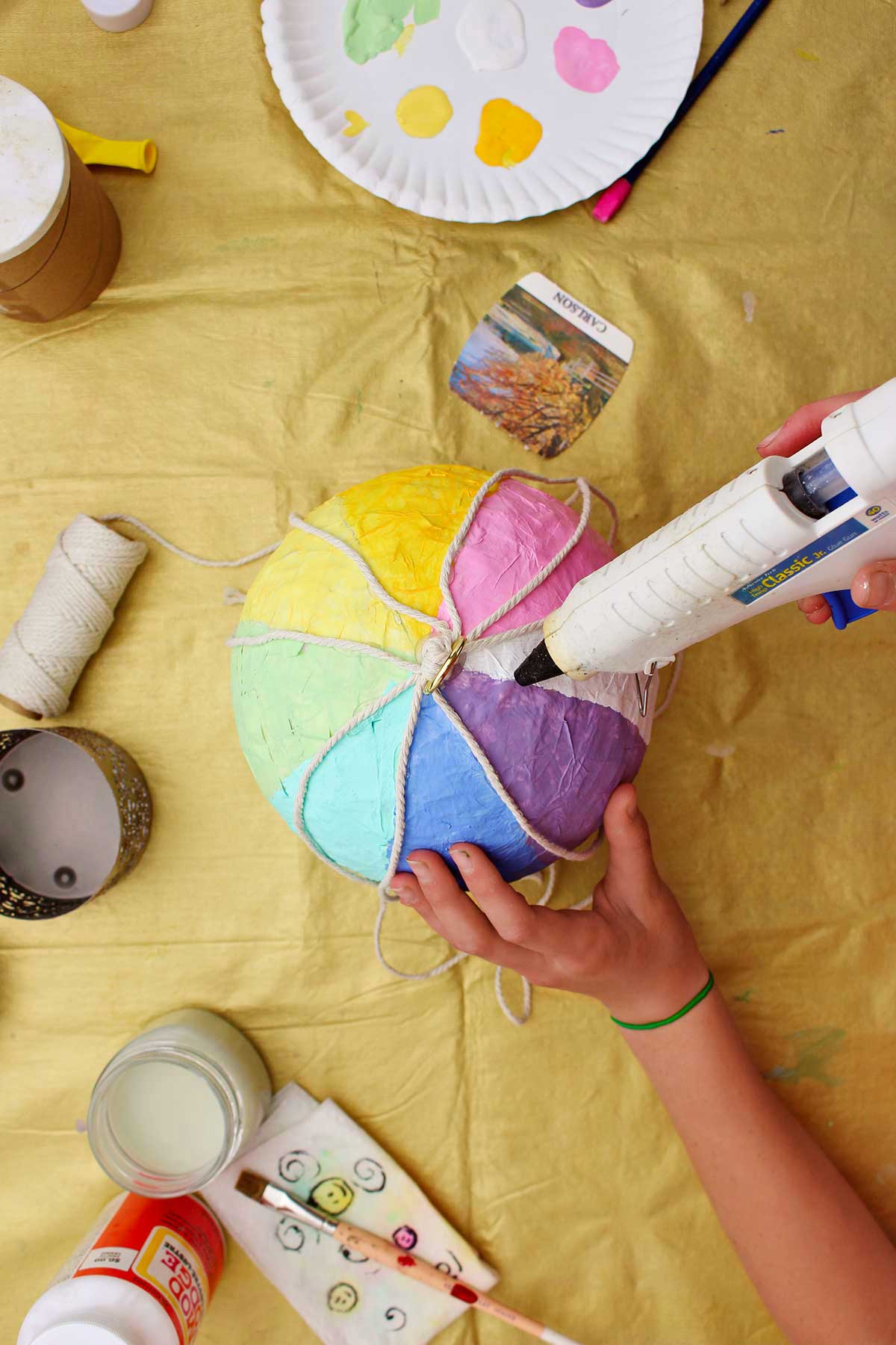 Pessoa colando pedaços de corda ao longo das listras pintadas em seu mini balão de ar quente.