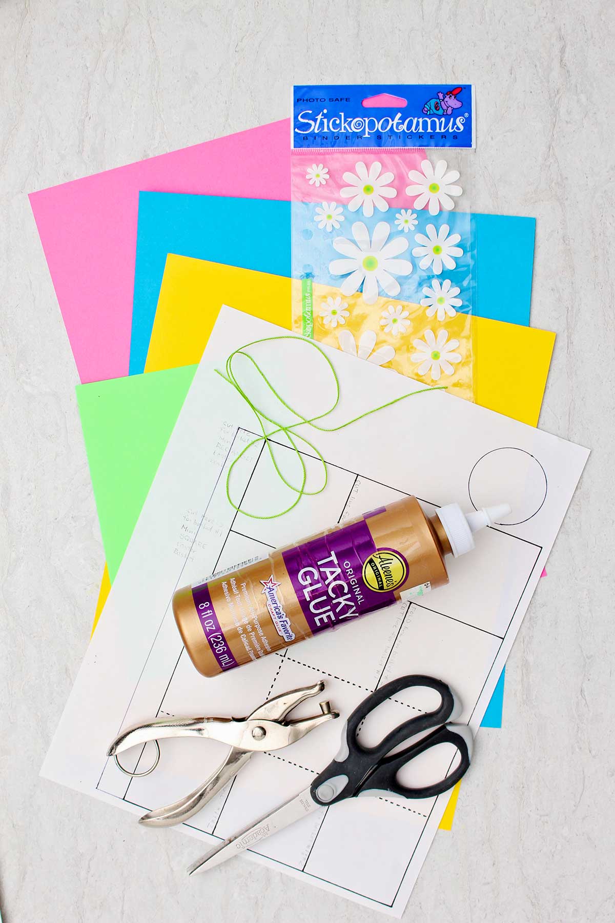 Um molde de mini cesto de Páscoa de papel, papel colorido, adesivos de flores, cola, tesoura e um perfurador.